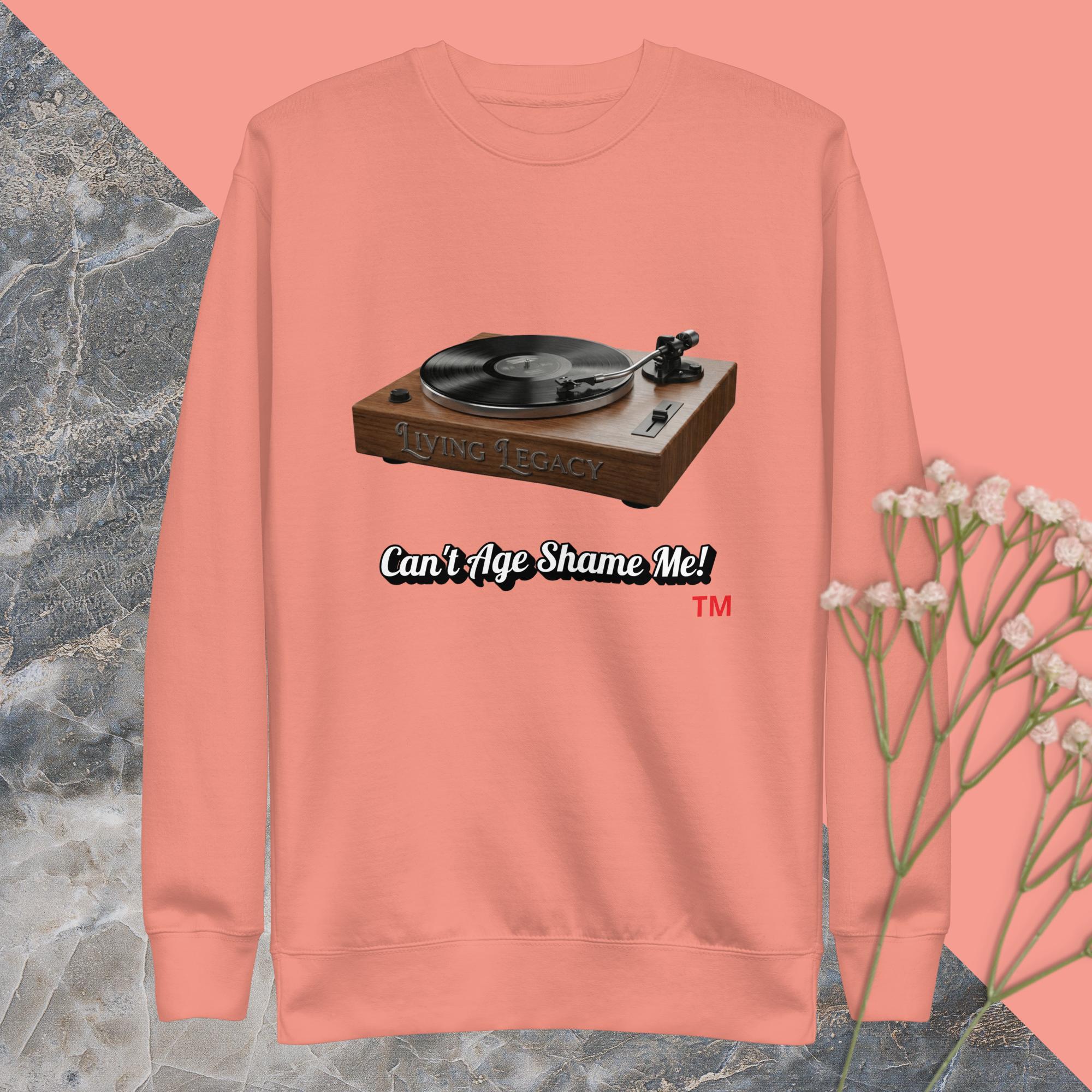 dusty rose sweatshirt with a record player graphic and text can't age shame me ! on a pink and gray background
