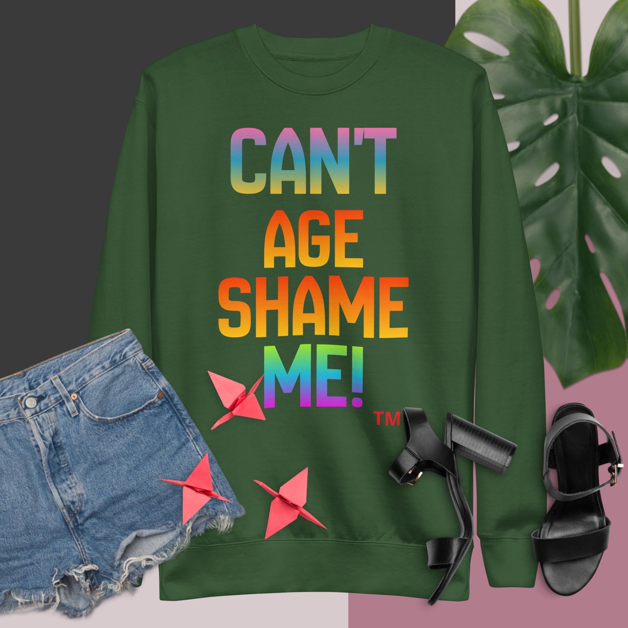 Green sweatshirt with colorful text, denim shorts, black sandals, and pink bows on a gradient background.