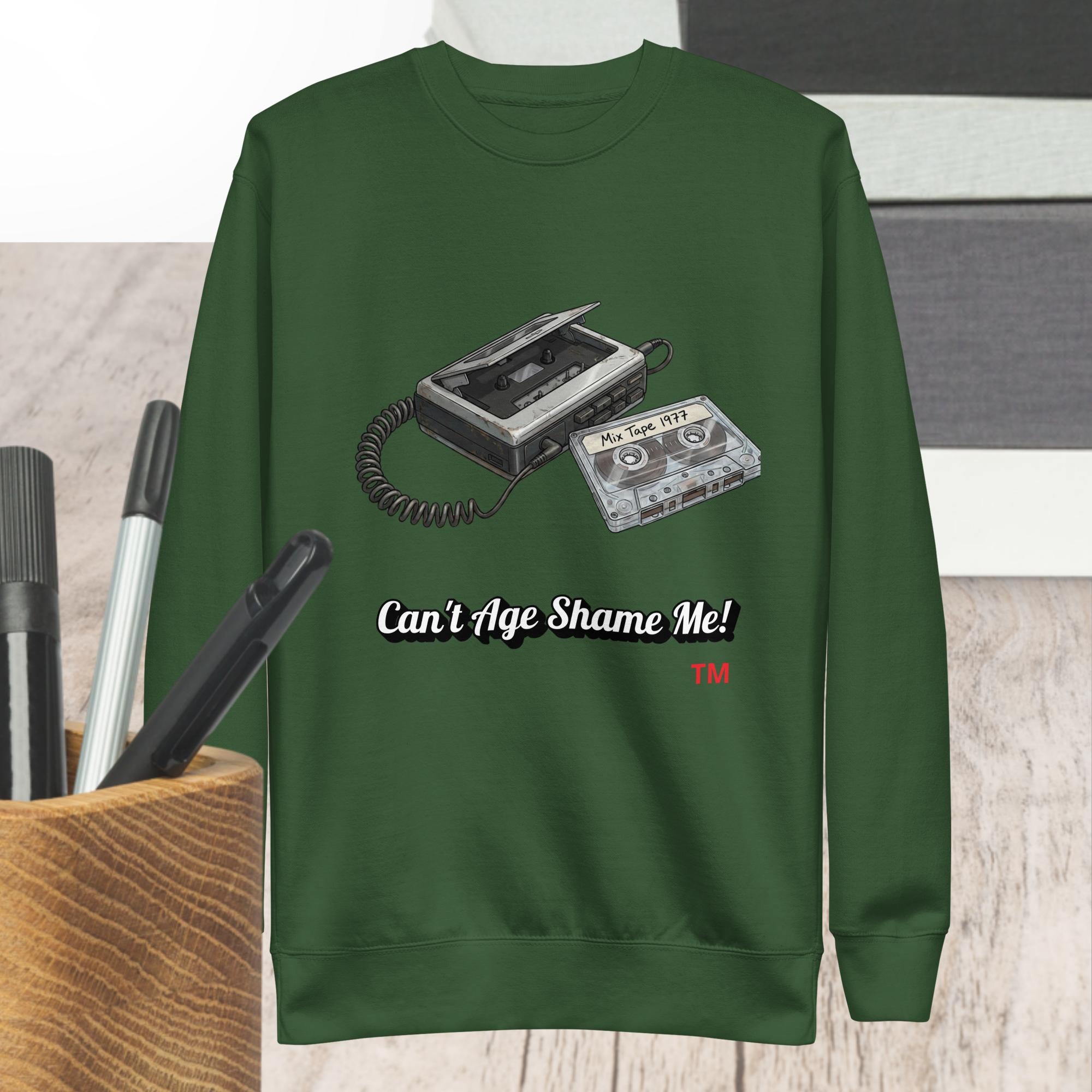 Green sweatshirt with a cassette tape design and text 'Can't Age Shame Me!' on a wooden surface.