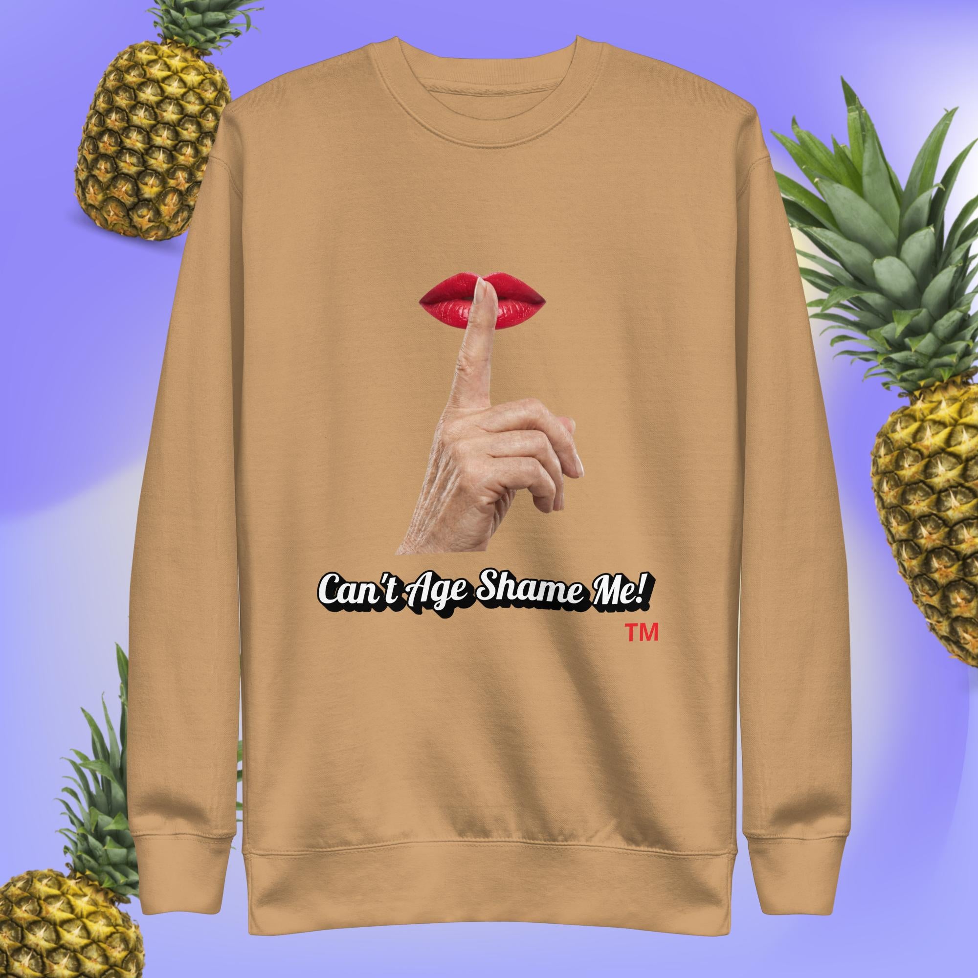 Khaki sweatshirt with a graphic design of finger on mouth and text 'Can't Age Shame Me!' on a blue background with pineapples.