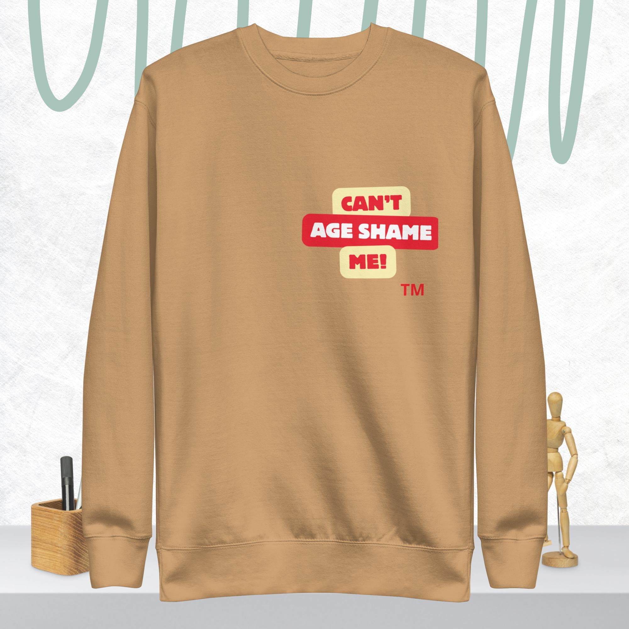 Khaki sweatshirt with 'CAN'T AGE SHAME ME!' text logo on a light gray background