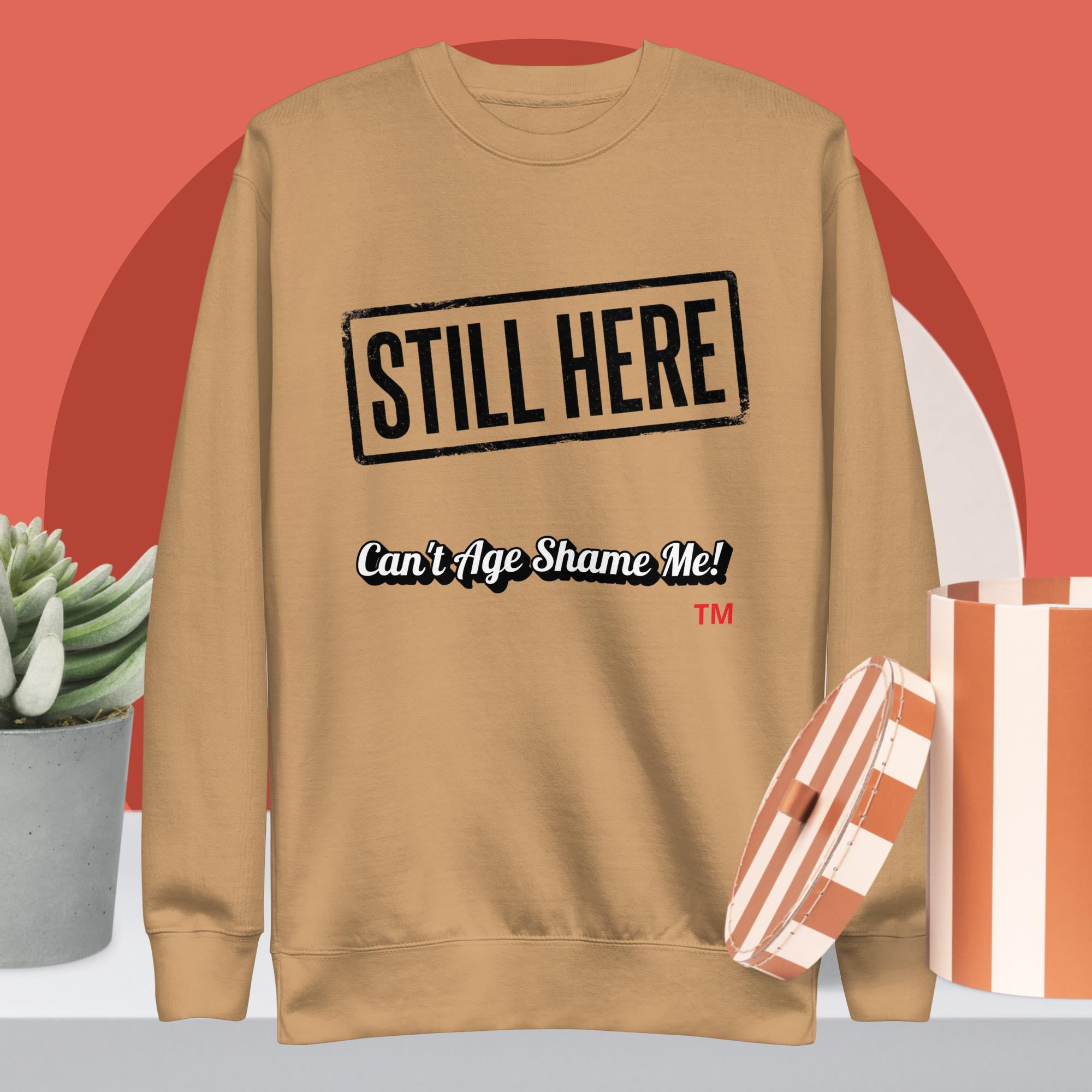 Khaki sweatshirt with 'STILL HERE Can't Age Shame Me!' text on a red background