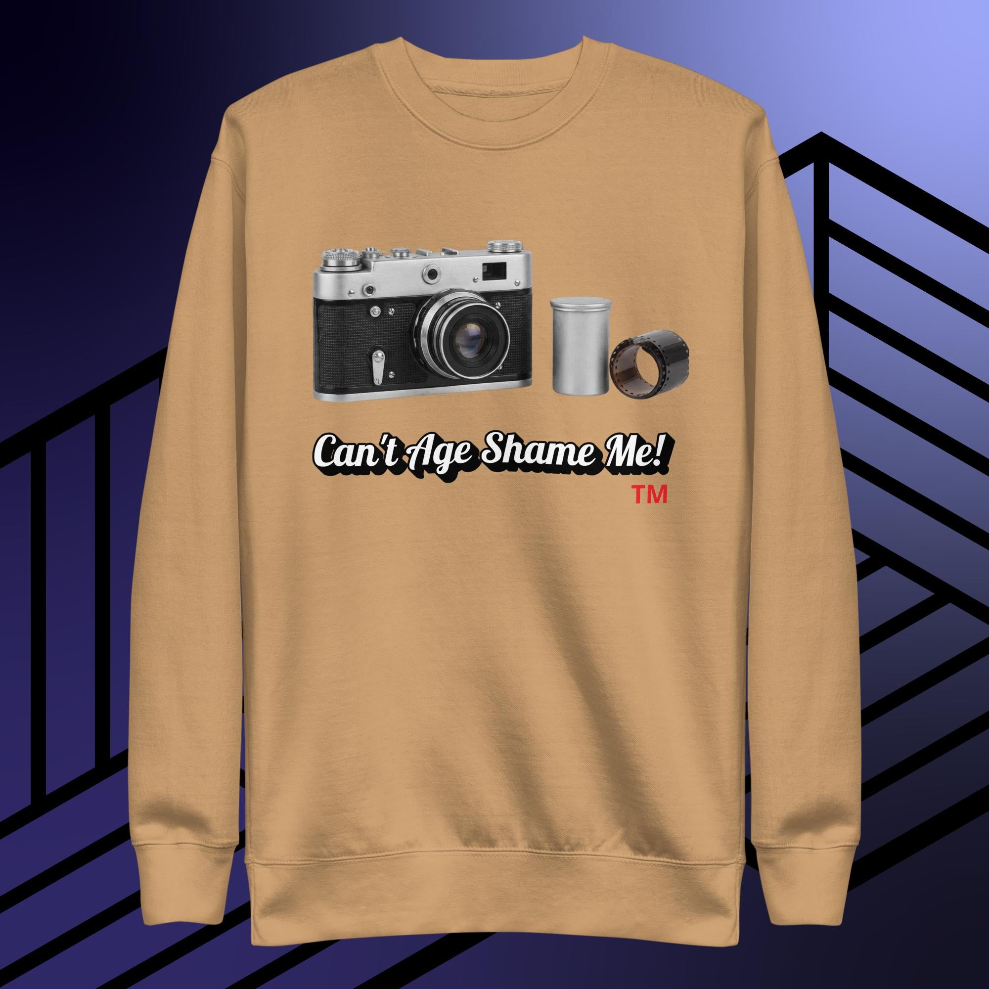 khaki sweatshirt with camera graphic and text can't age shame me! on a blue and black striped background.