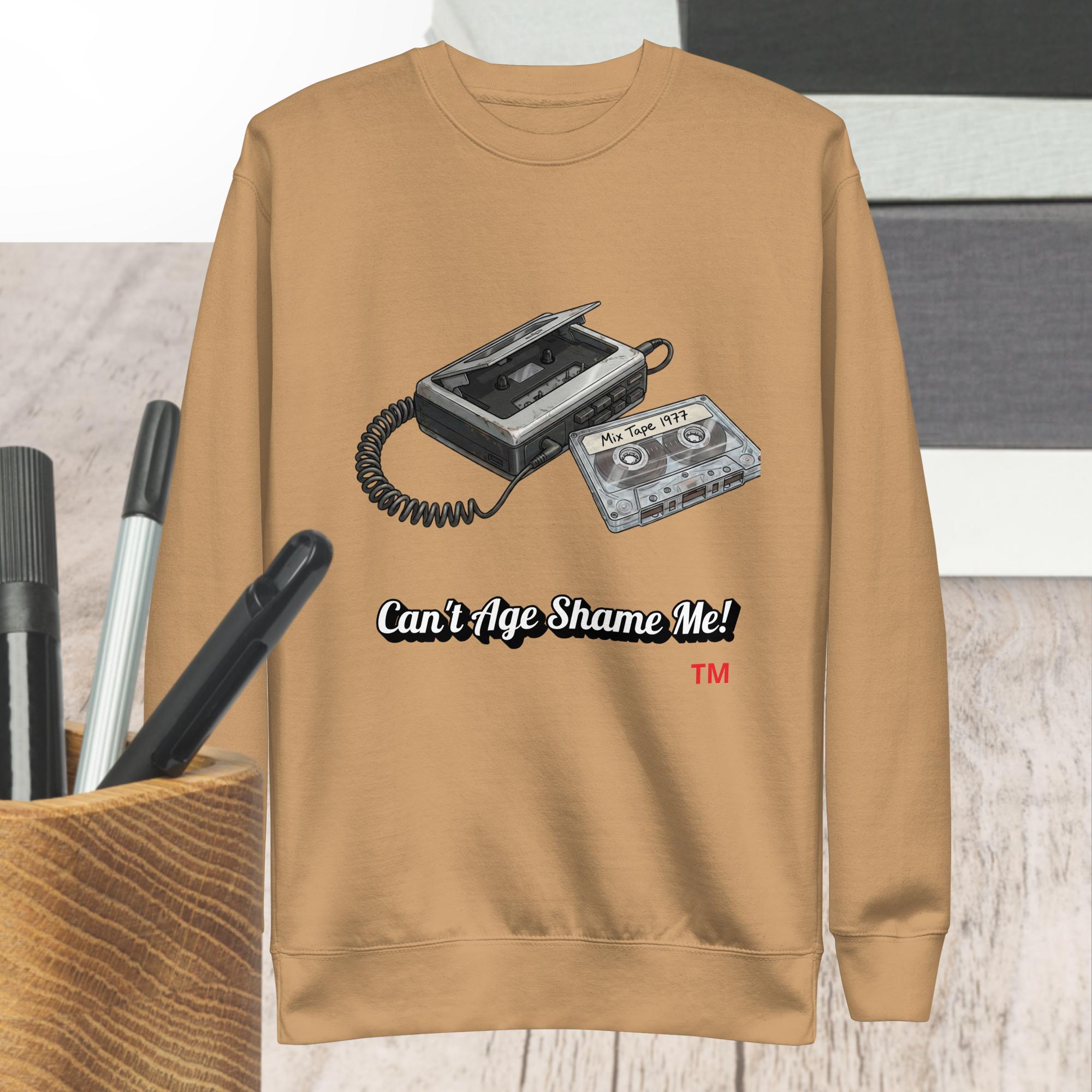 khaki sweatshirt with cassette tape design and text 'Can't Age Shame Me!' on a wooden surface.