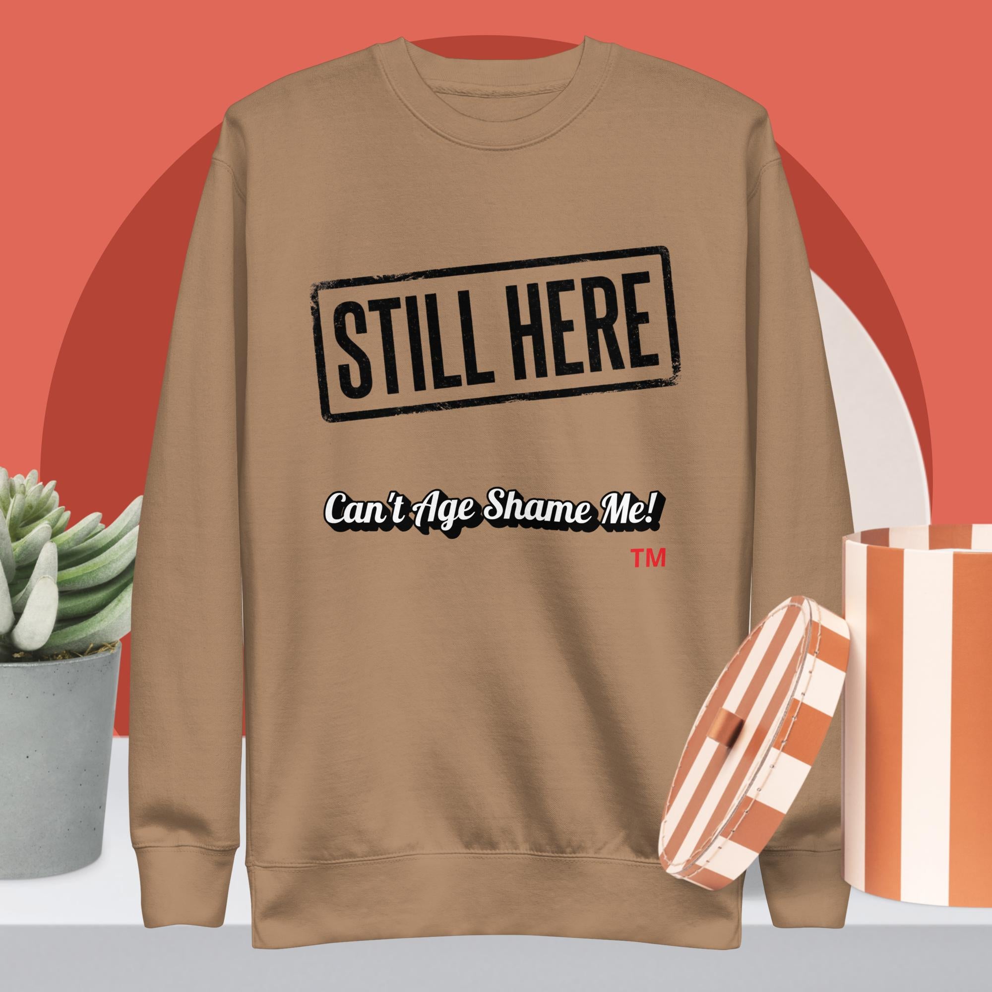 Latte sweatshirt with 'STILL HERE Can't Age Shame Me!' text on a red background