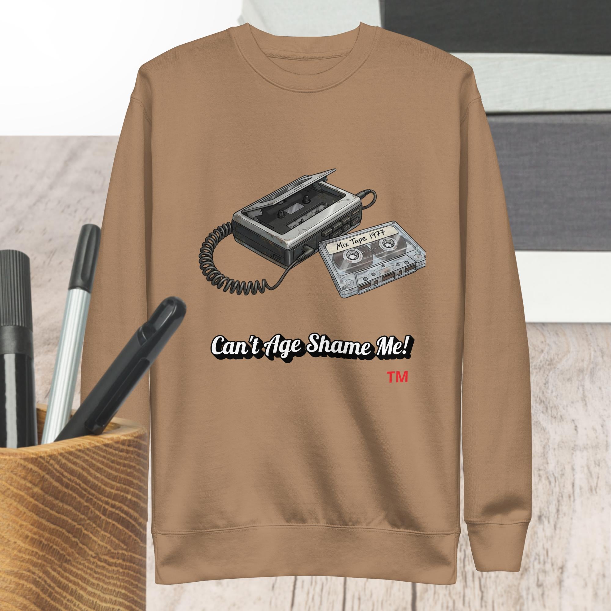 latte sweatshirt with cassette tape design and text 'Can't Age Shame Me!' on a wooden surface.
