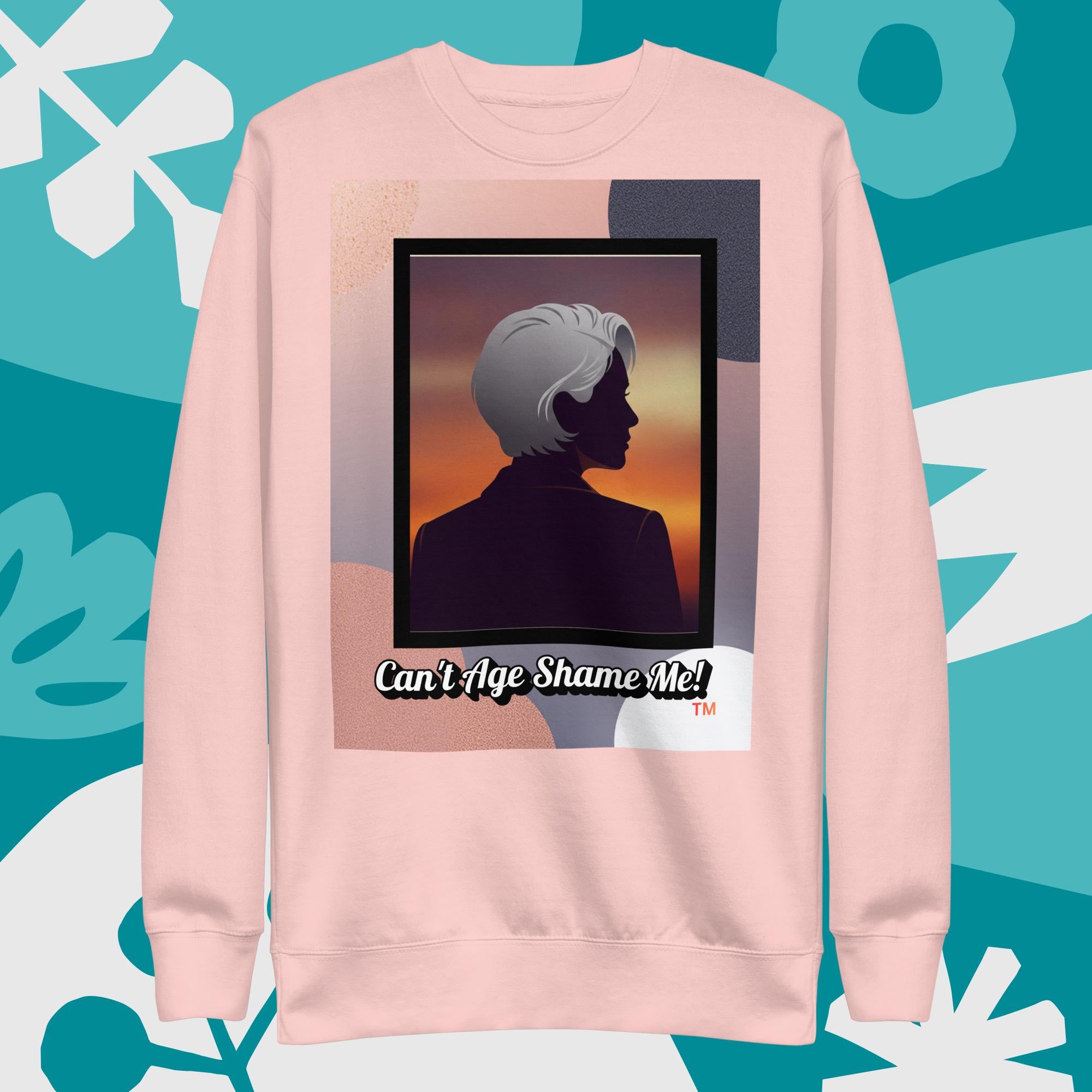 Light Pink sweatshirt with a graphic design featuring a woman with gray hair silhouette and text: Can’t Age Shame Me! surrounded by decorative plants on a light gray background.

