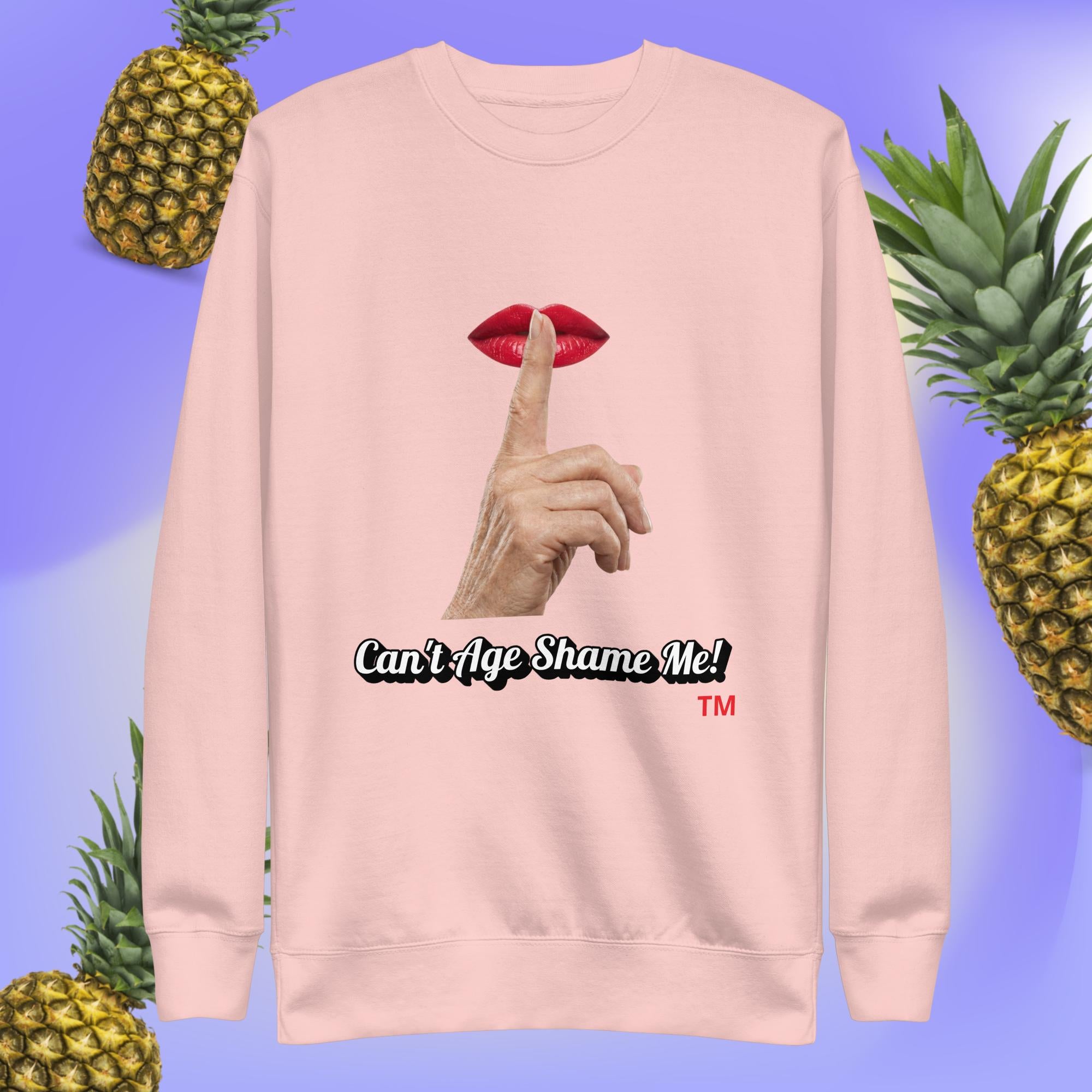 Light Pink  sweatshirt with a graphic design of finger on mouth and text 'Can't Age Shame Me!' on a blue background with pineapples.