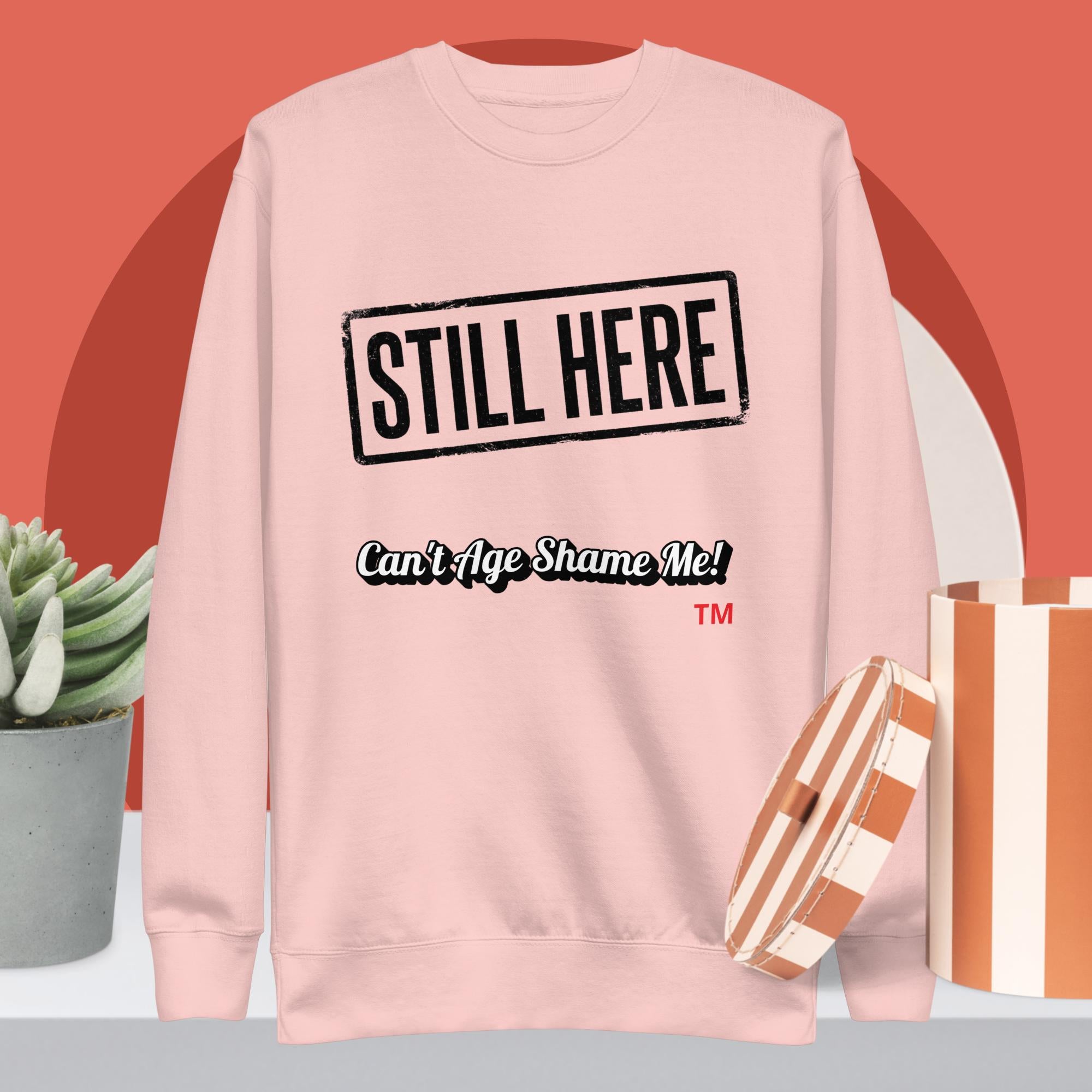 Pink sweatshirt with 'STILL HERE Can't Age Shame Me!' text on a red background