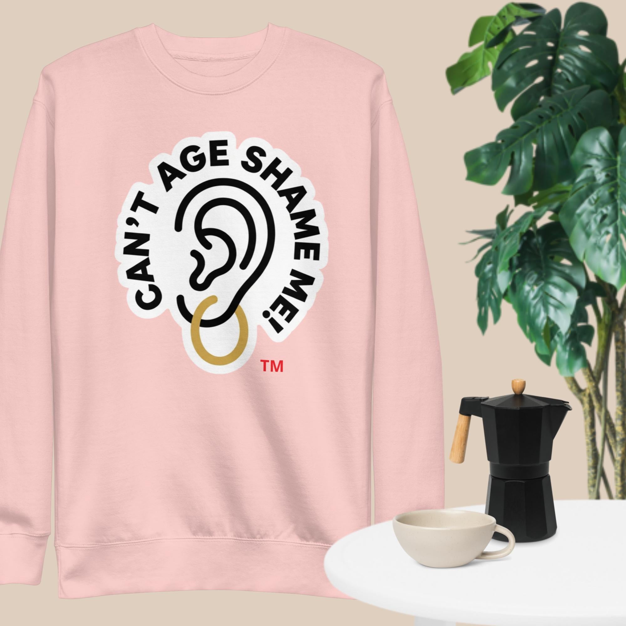 Light Pink sweatshirt with 'Can't Age Shame Me' graphic on a beige background with a plant and coffee set.