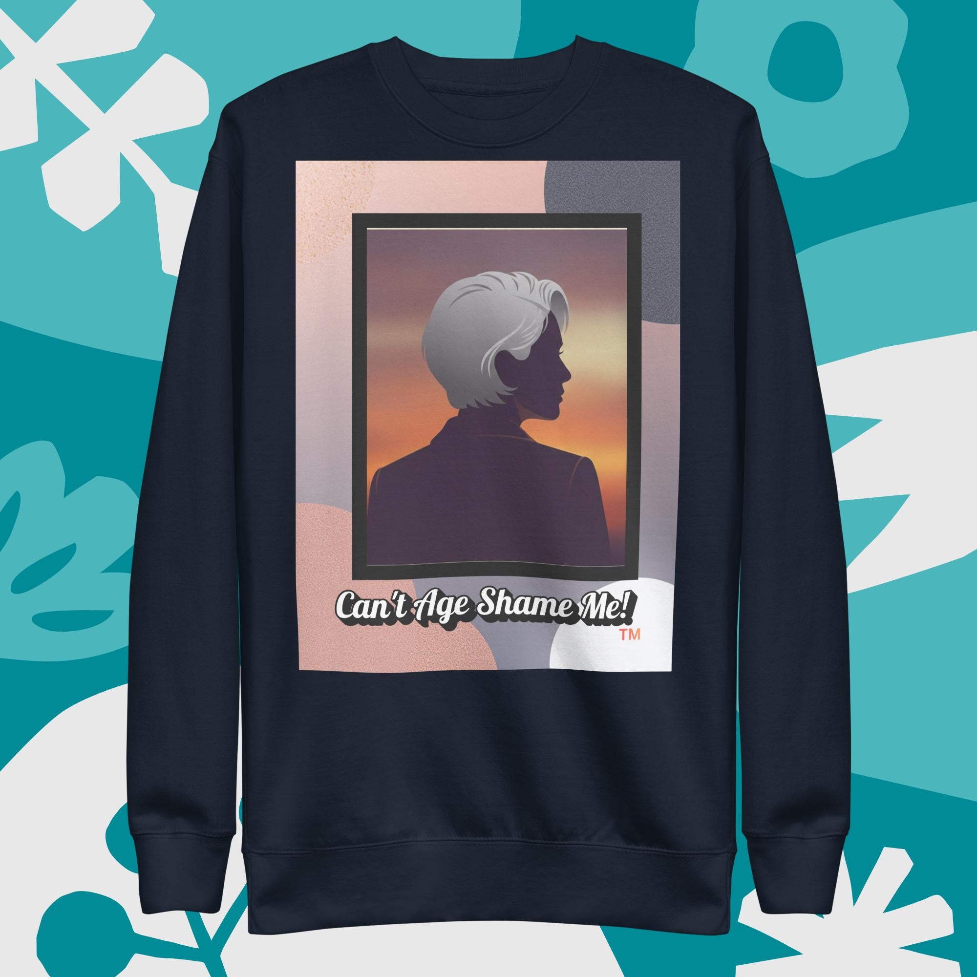 Navy sweatshirt with a graphic design featuring a woman with gray hair silhouette and text: Can’t Age Shame Me! surrounded by decorative plants on a light gray background.

