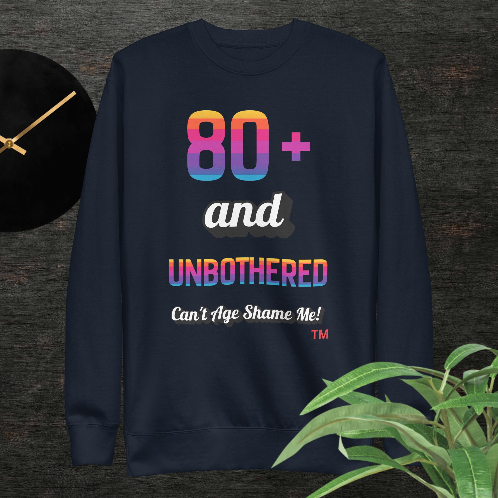 Navy blue sweatshirt with colorful text design on a dark surface with a clock and plant.