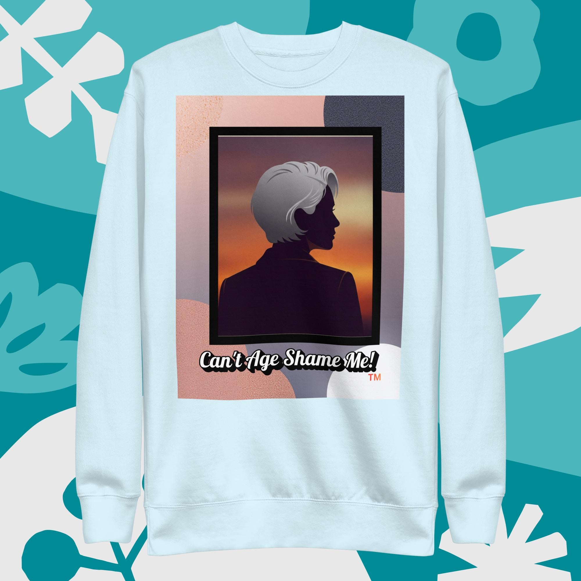 Sky Blue sweatshirt with a graphic design featuring a woman with gray hair silhouette and text: Can’t Age Shame Me! surrounded by decorative plants on a light gray background.

