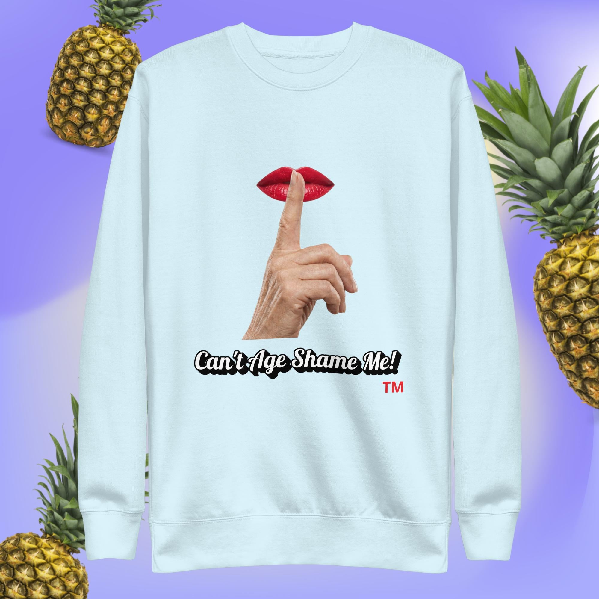 Sky Blue sweatshirt with a graphic design of finger on mouth and text 'Can't Age Shame Me!' on a blue background with pineapples.