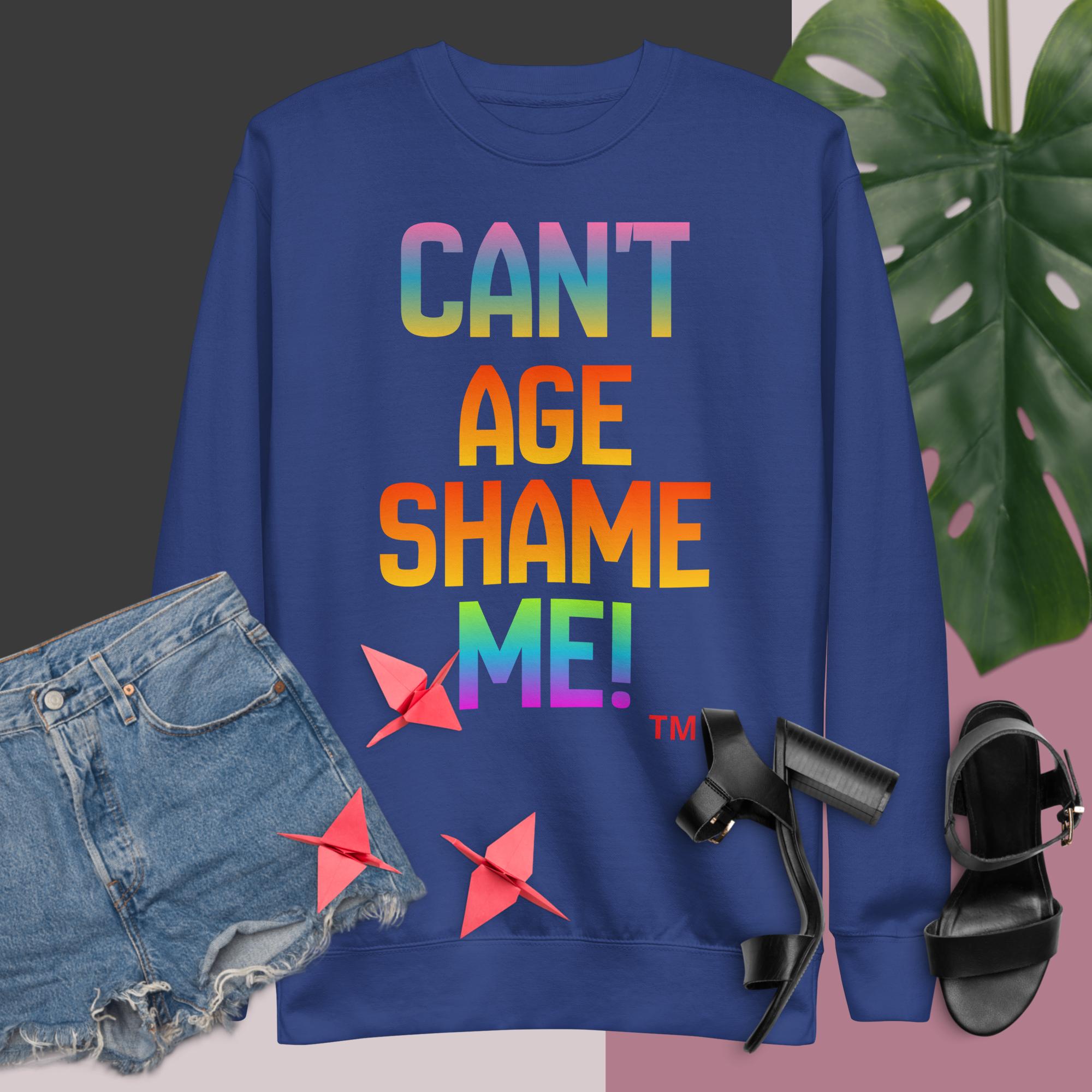 Blue sweatshirt with colorful text, denim shorts, black sandals, and a plant on a pink and gray background