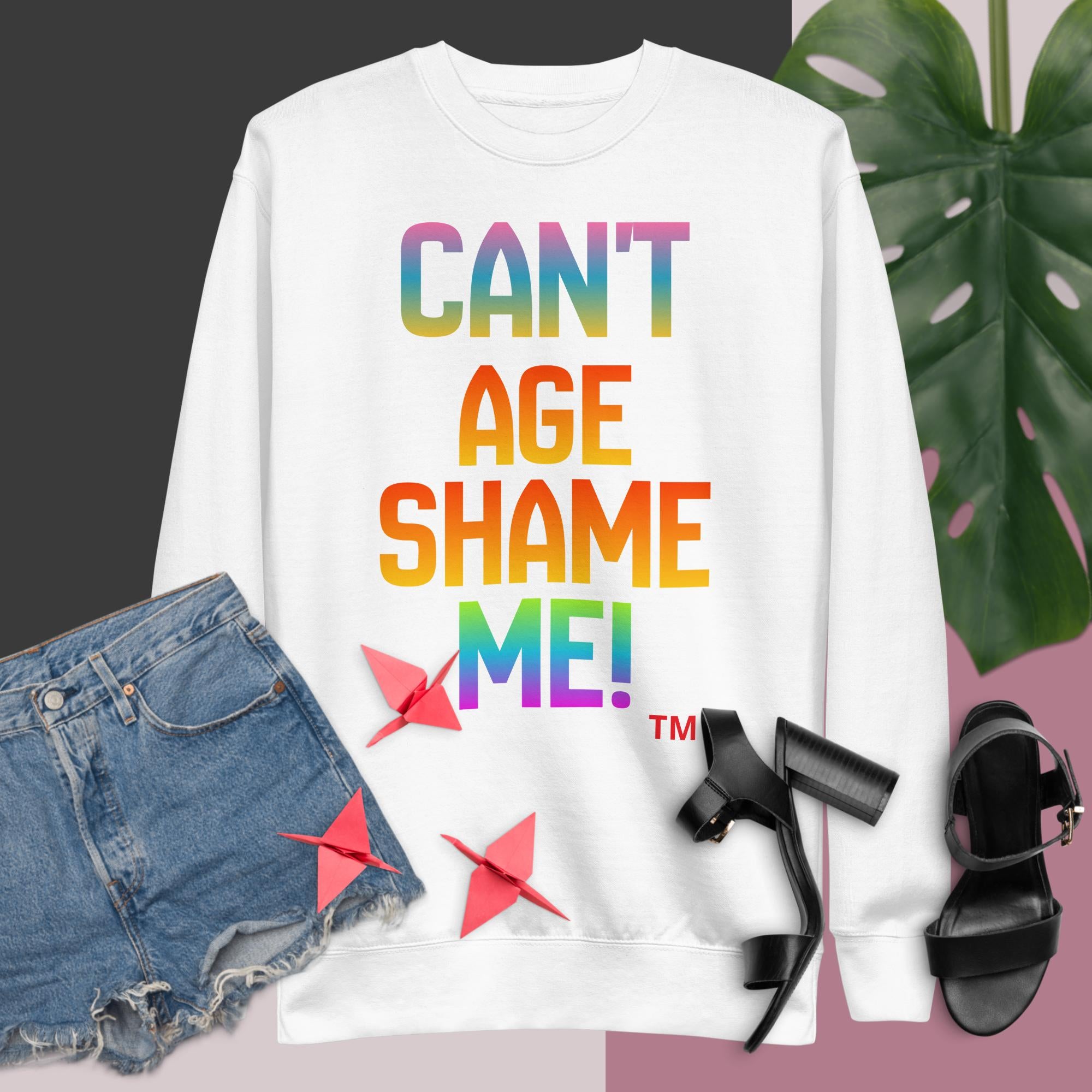 White sweatshirt with colorful text 'CAN'T AGE SHAME ME!' displayed with denim shorts and black high-heeled shoes.
