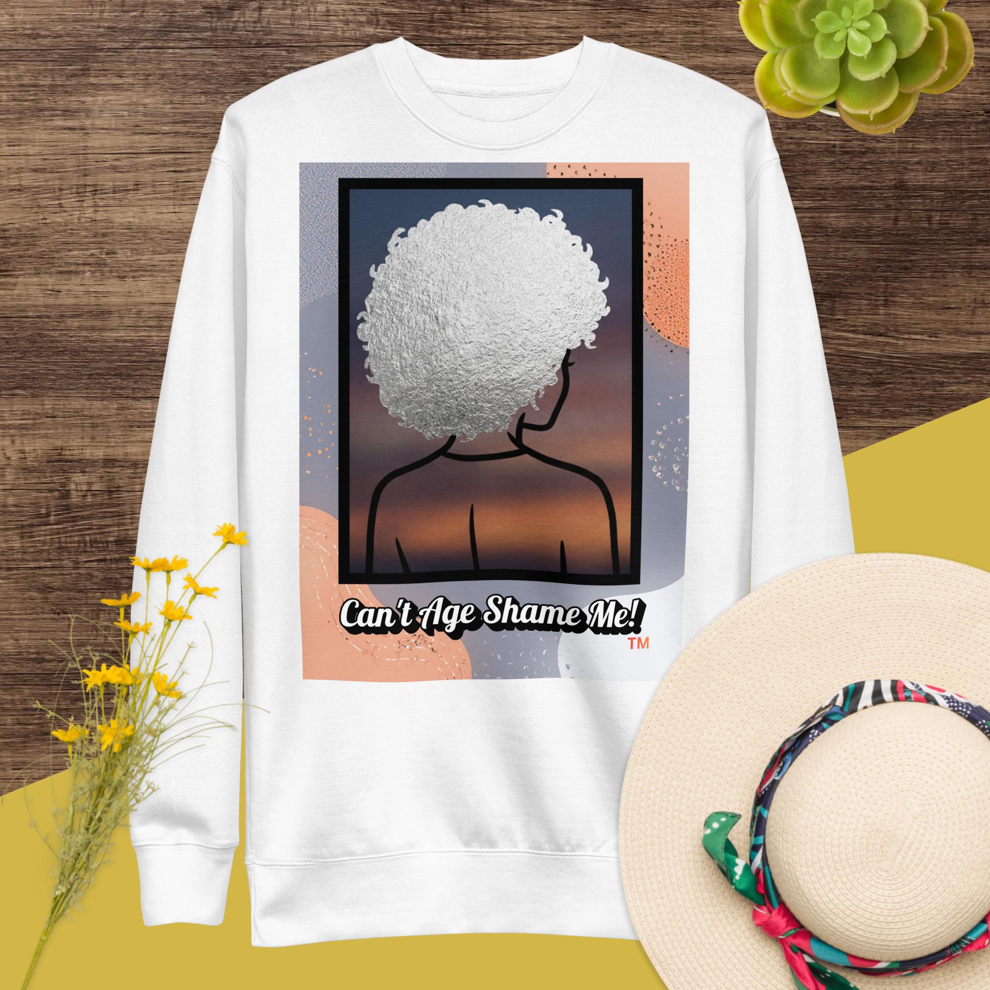 White sweatshirt with a graphic design of a person with textured hair and text 'Can't Age Shame Me!' on a colorful background.