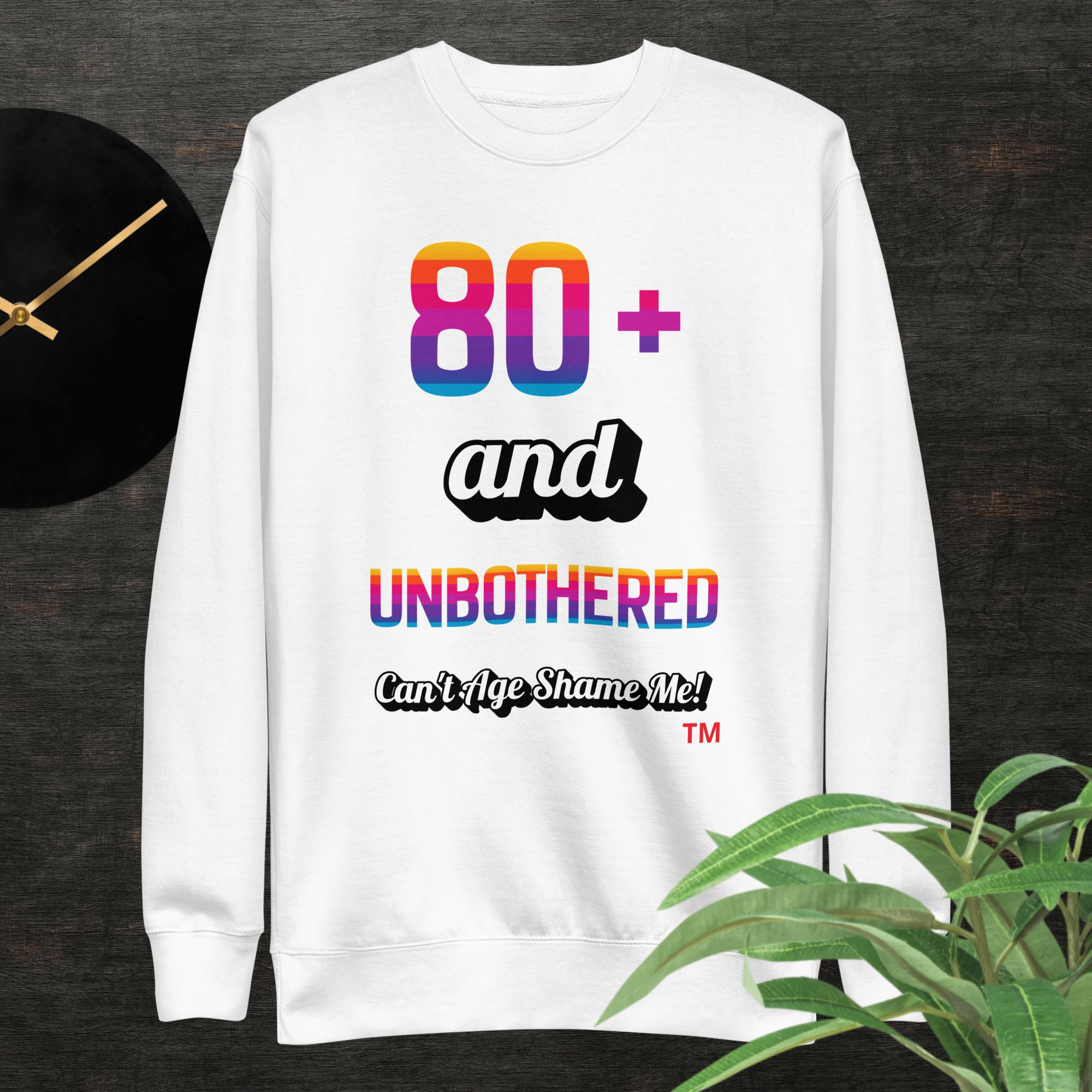 White sweatshirt with colorful text design on a dark surface with a clock and plant.