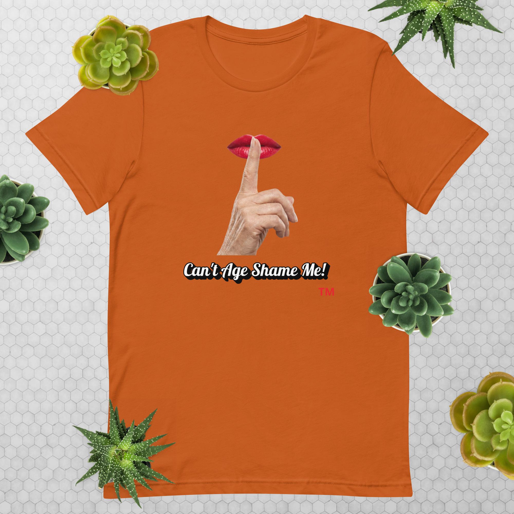 Autumn t-shirt with graphic design of finger on mouth and text 'CAN'T AGE SHAME ME!' text logo on a light gray background with succulents.