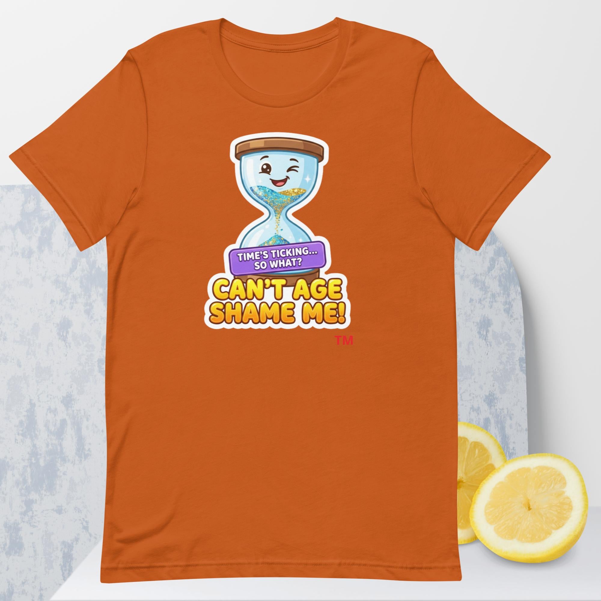 Autumn t-shirt with a cartoon hourglass design and text 'Can't Age Shame Me' graphic on a light gray background.

