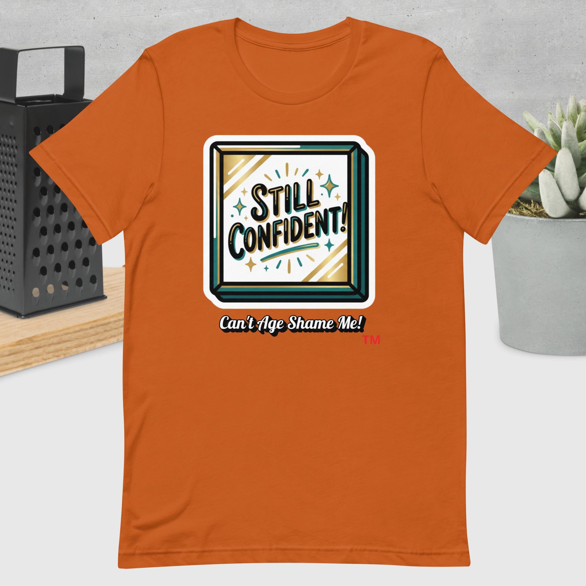 Autumn t-shirt with 'Still Confident! Can't Age Shame Me!' graphic design on a neutral background.