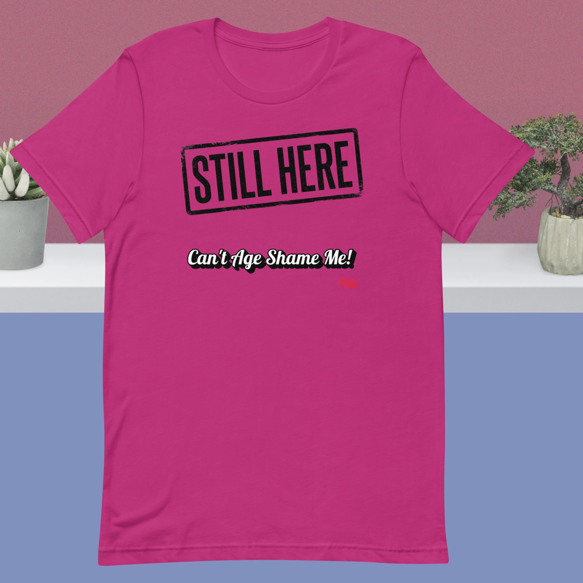 Berry t-shirt with 'STILL HERE Can't Age Shame Me!' text on a pink and blue gradient background.