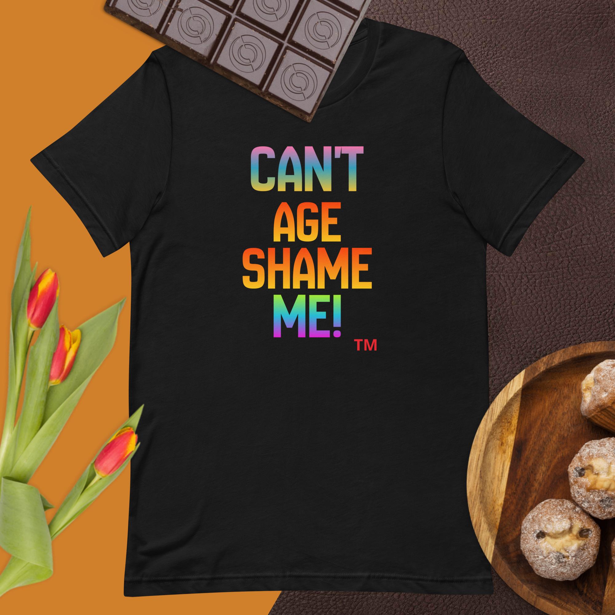 Black t-shirt with colorful text 'CAN'T AGE SHAME ME!' on a brown background with chocolate and flowers.