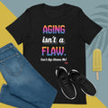 Black t-shirt with 'Aging isn't a flaw' text, paired with jeans and sneakers on a colorful background.