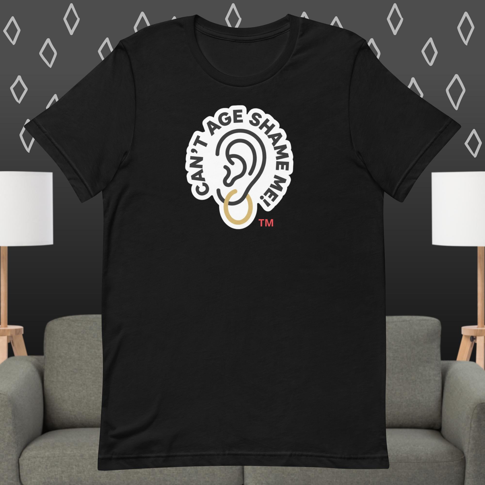 Black  t-shirt with 'Can't Age Shame Me' graphic on a gray couch and lamp background