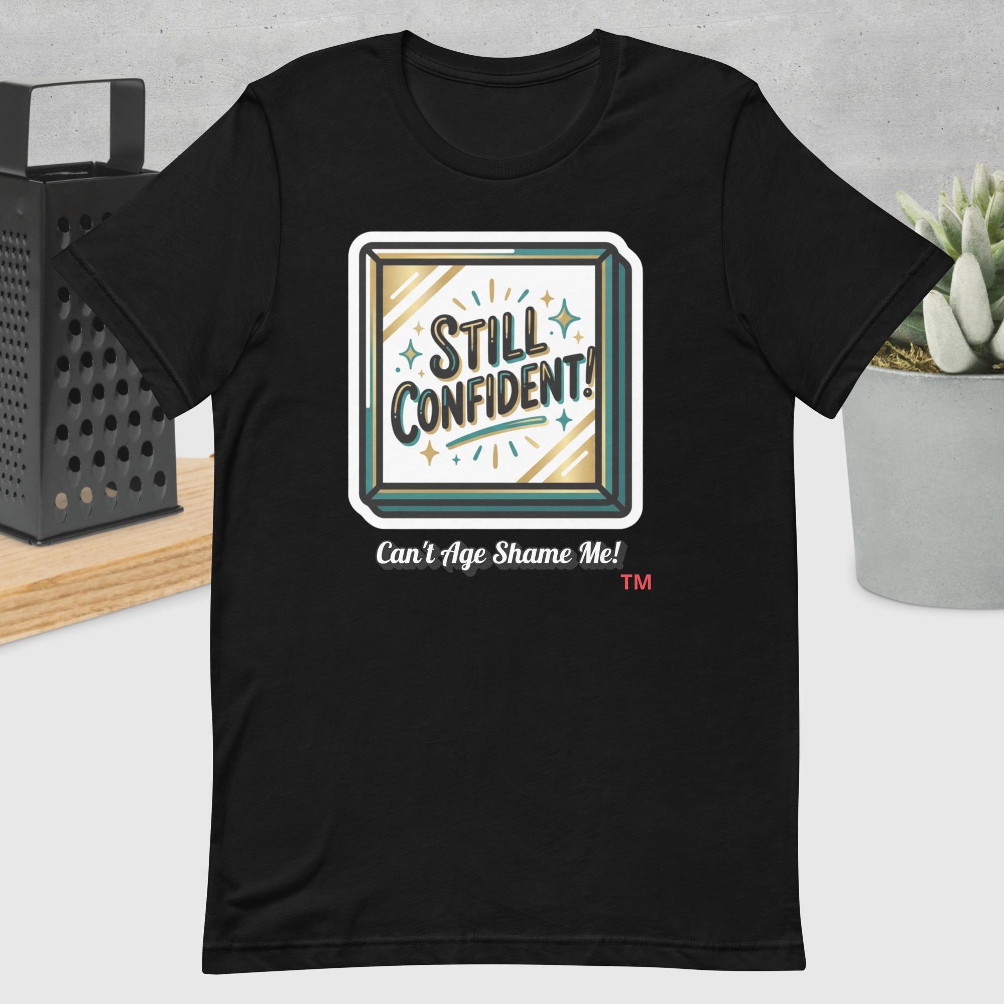 Black t-shirt with 'Still Confident! Can't Age Shame Me!' graphic design on a neutral background