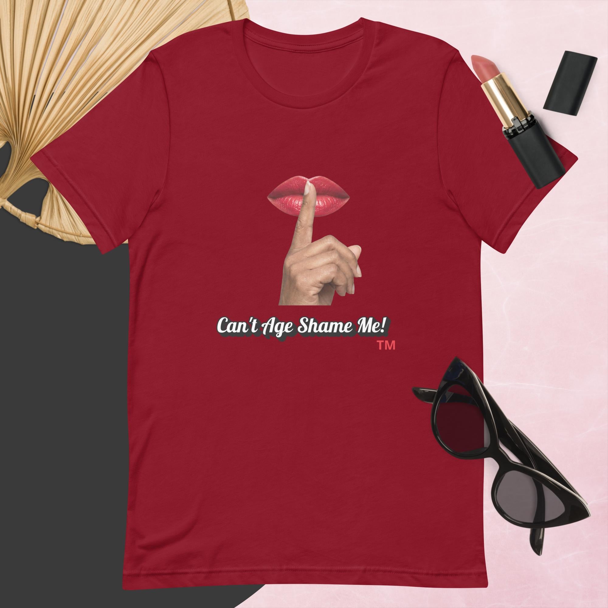 Cardinal t-shirt with graphic design and text, Can’t Age Shame Me!,   surrounded by sunglasses, lipstick, and a fan on a pink background.

 


 

