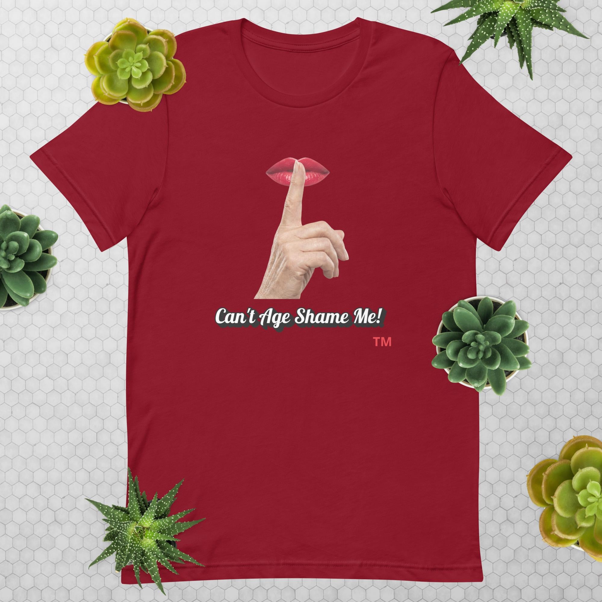 Cardinal t-shirt with graphic design of finger on mouth and text 'CAN'T AGE SHAME ME!' text logo on a light gray background with succulents.