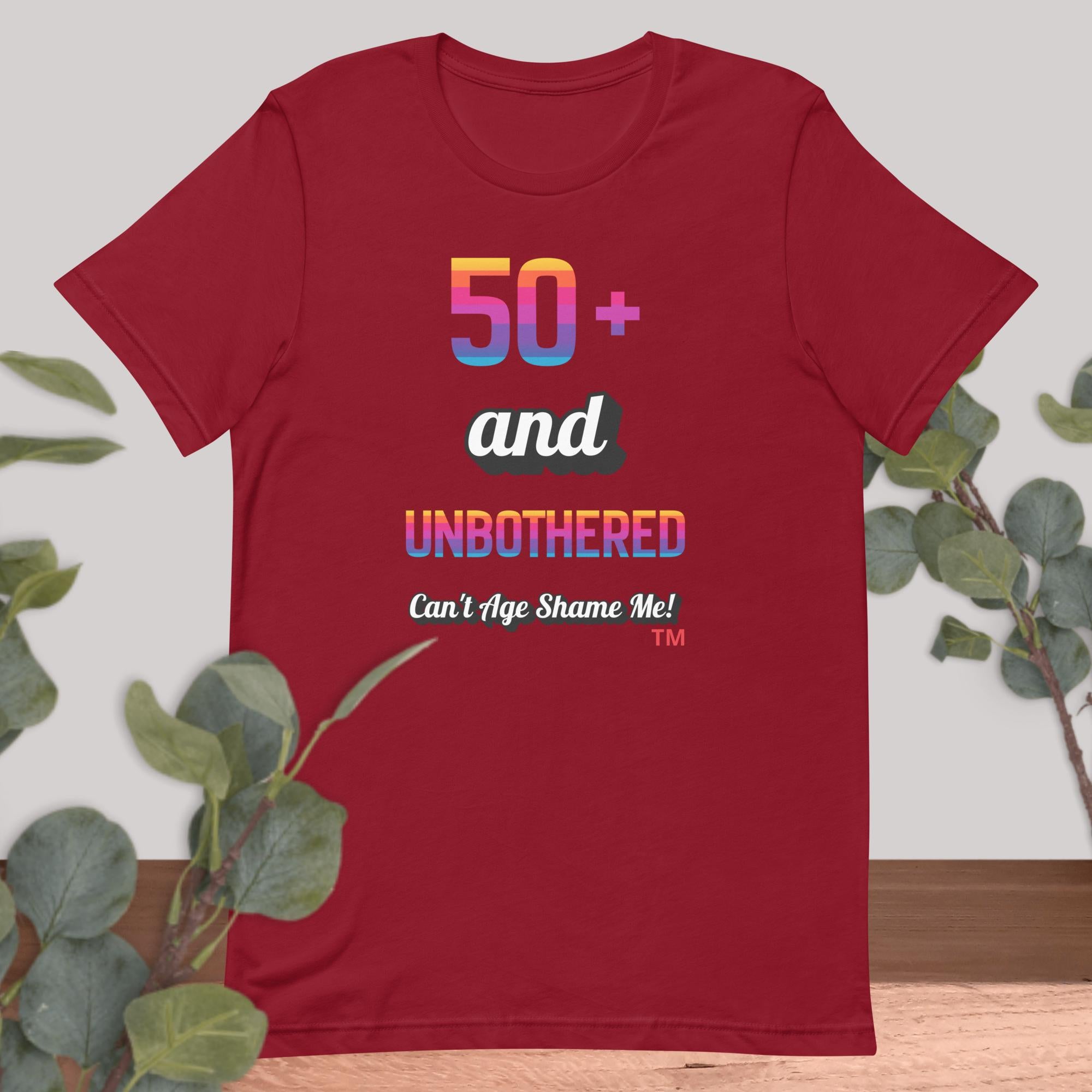Red t-shirt with colorful text design on a light background with green leaves.