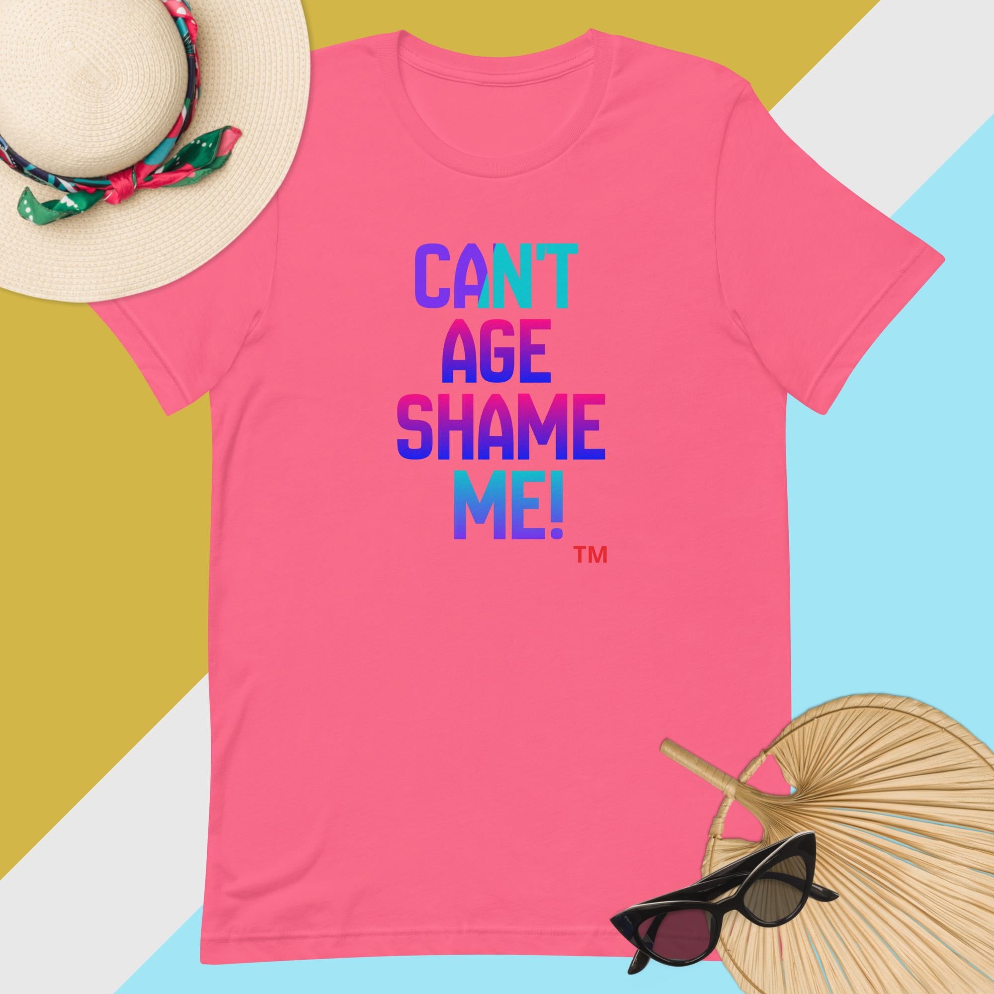 Pink t-shirt with 'CAN'T AGE SHAME ME!' text on a colorful background with hat, sunglasses, and fan.