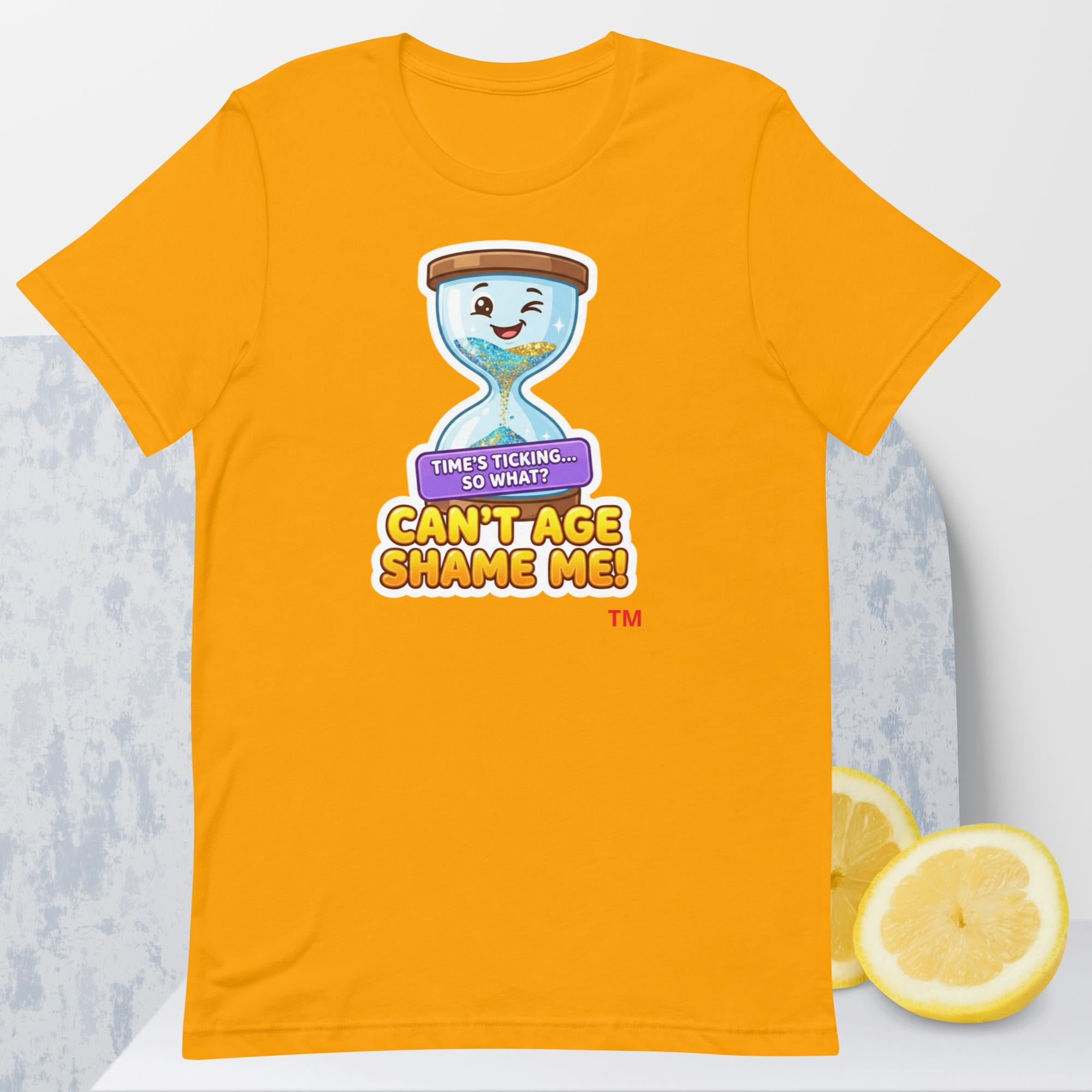 Gold t-shirt with a cartoon hourglass design and text 'Can't Age Shame Me' graphic on a light gray background.

