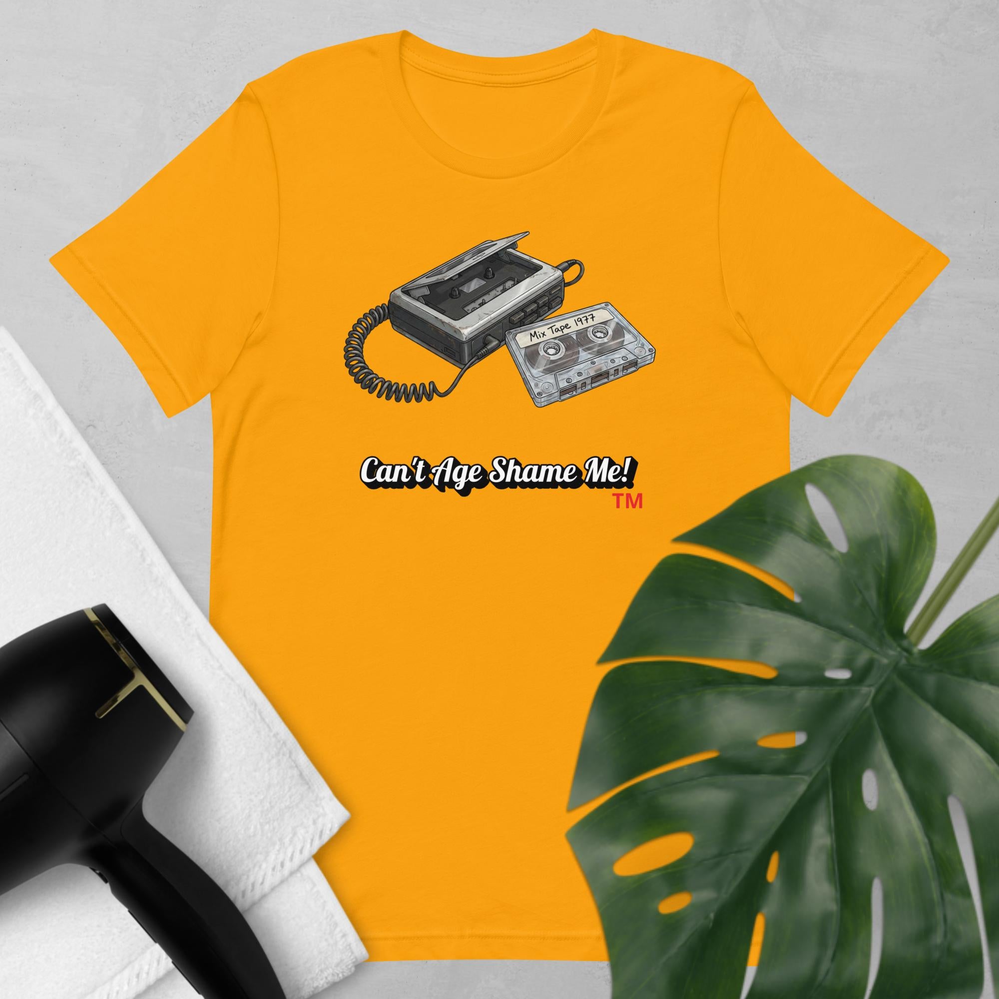 gold t-shirt with cassette tape design and text 'Can't Age Shame Me!' on a light gray background.