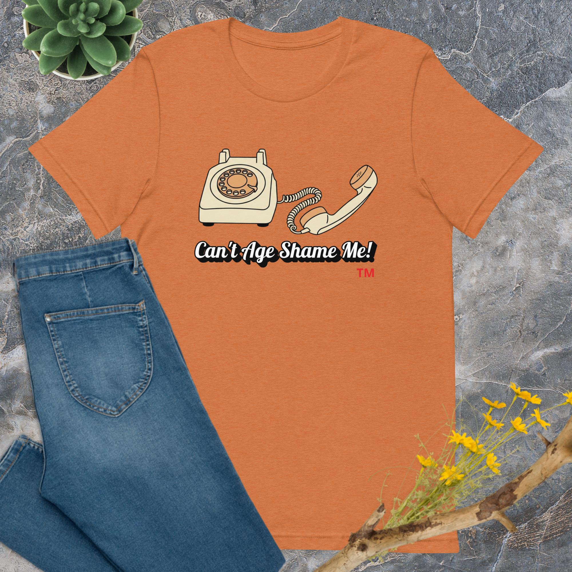 heather autumn t-shirt with phone graphic and text 'Can't Age Shame Me!' on a gray surface with jeans and plant.