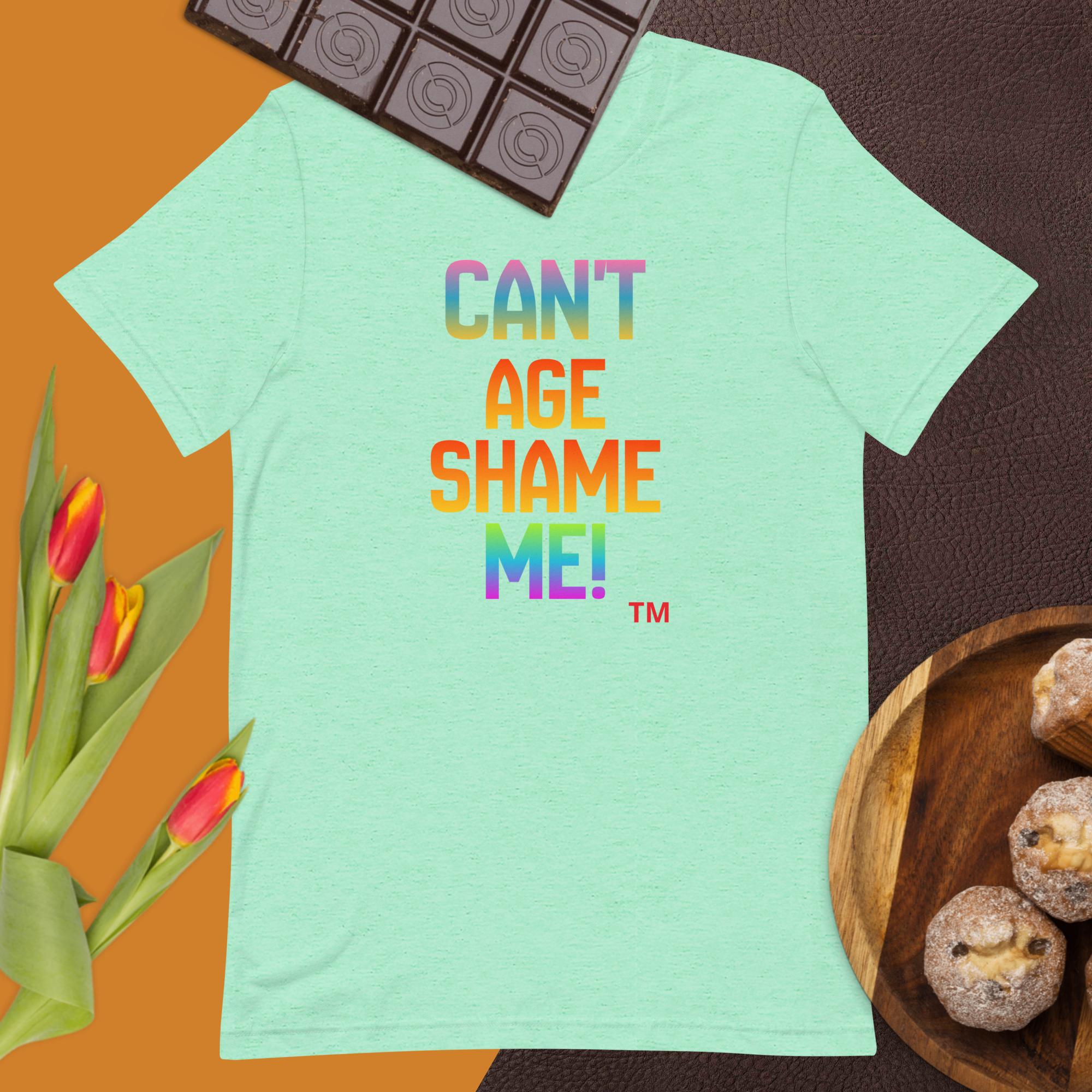 Light green t-shirt with colorful text 'CAN'T AGE SHAME ME!' on a brown background with chocolate and tulips.
