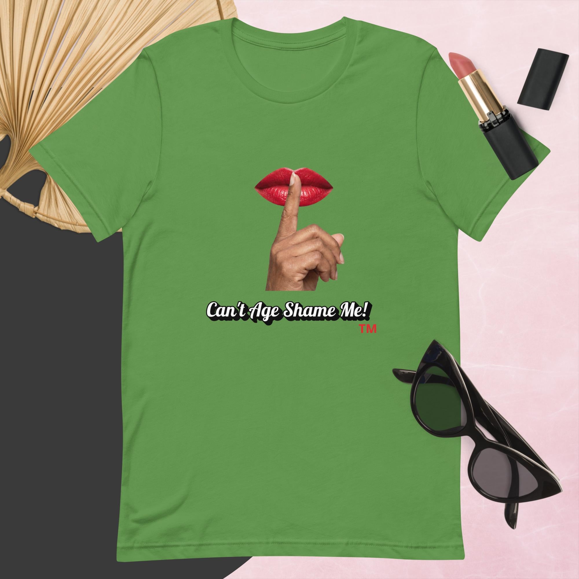 Leaf t-shirt with graphic design and text, Can’t Age Shame Me!,   surrounded by sunglasses, lipstick, and a fan on a pink background.

 
