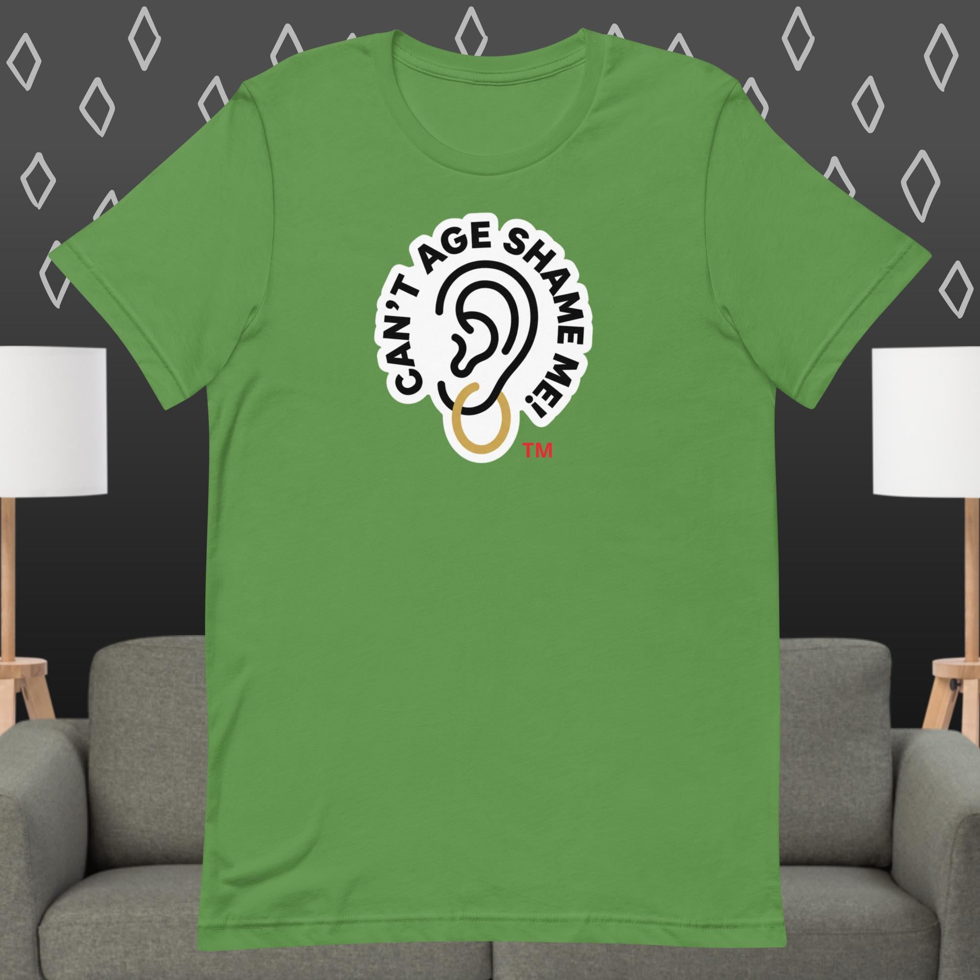 Green t-shirt with 'Can't Age Shame Me' graphic on a gray couch and lamp background