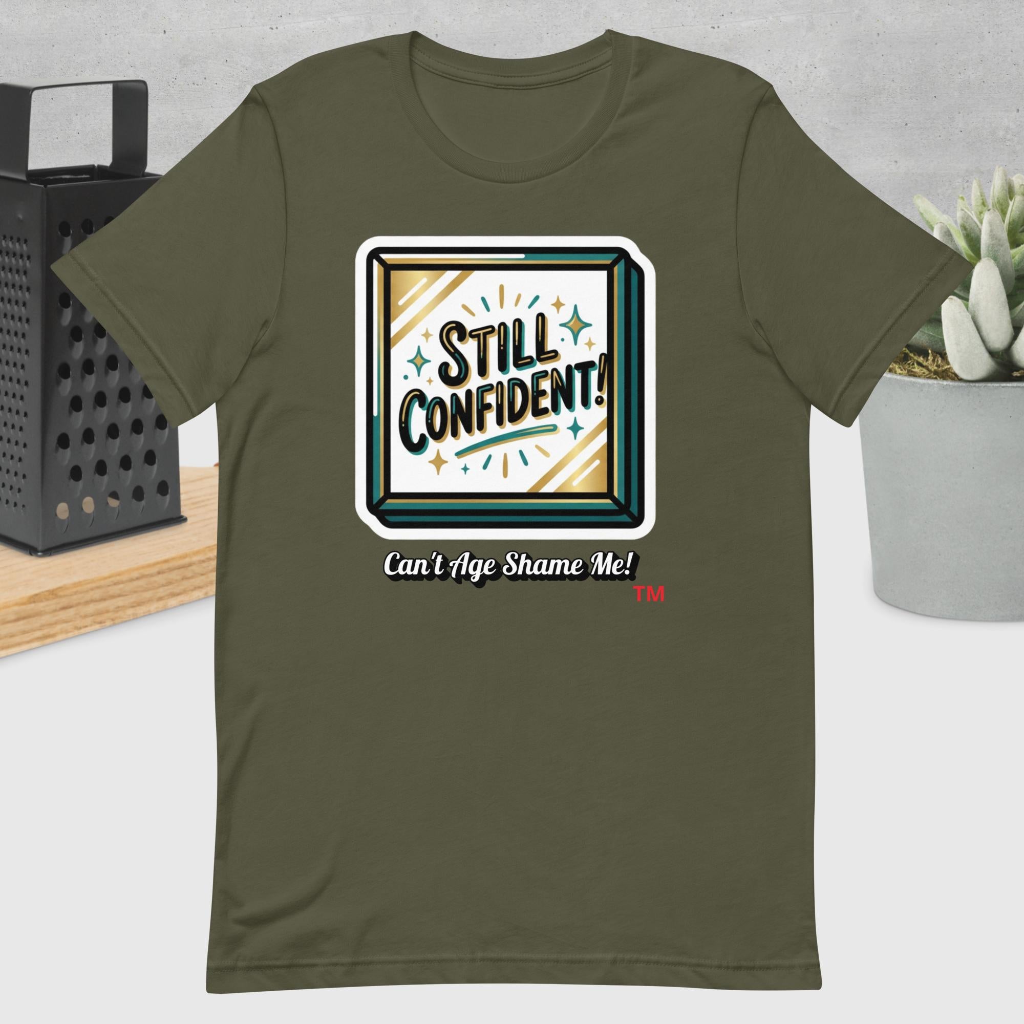 Military Green t-shirt with 'Still Confident! Can't Age Shame Me!' graphic design on a neutral background.