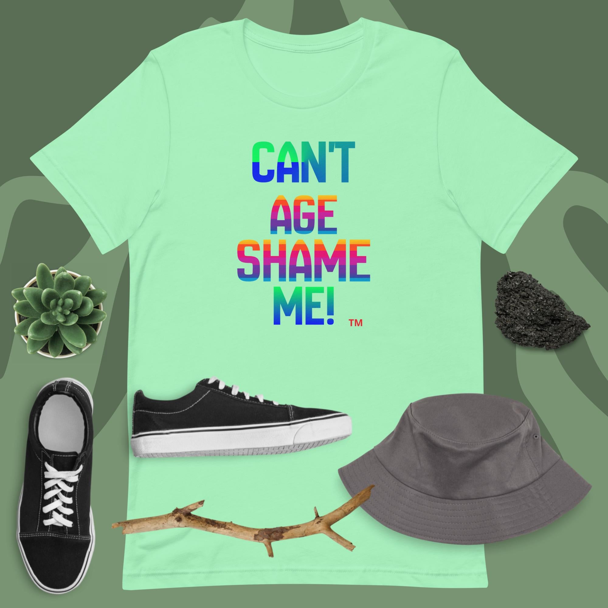Mint green t-shirt with colorful text, black sneakers, gray bucket hat, and branch on a green background