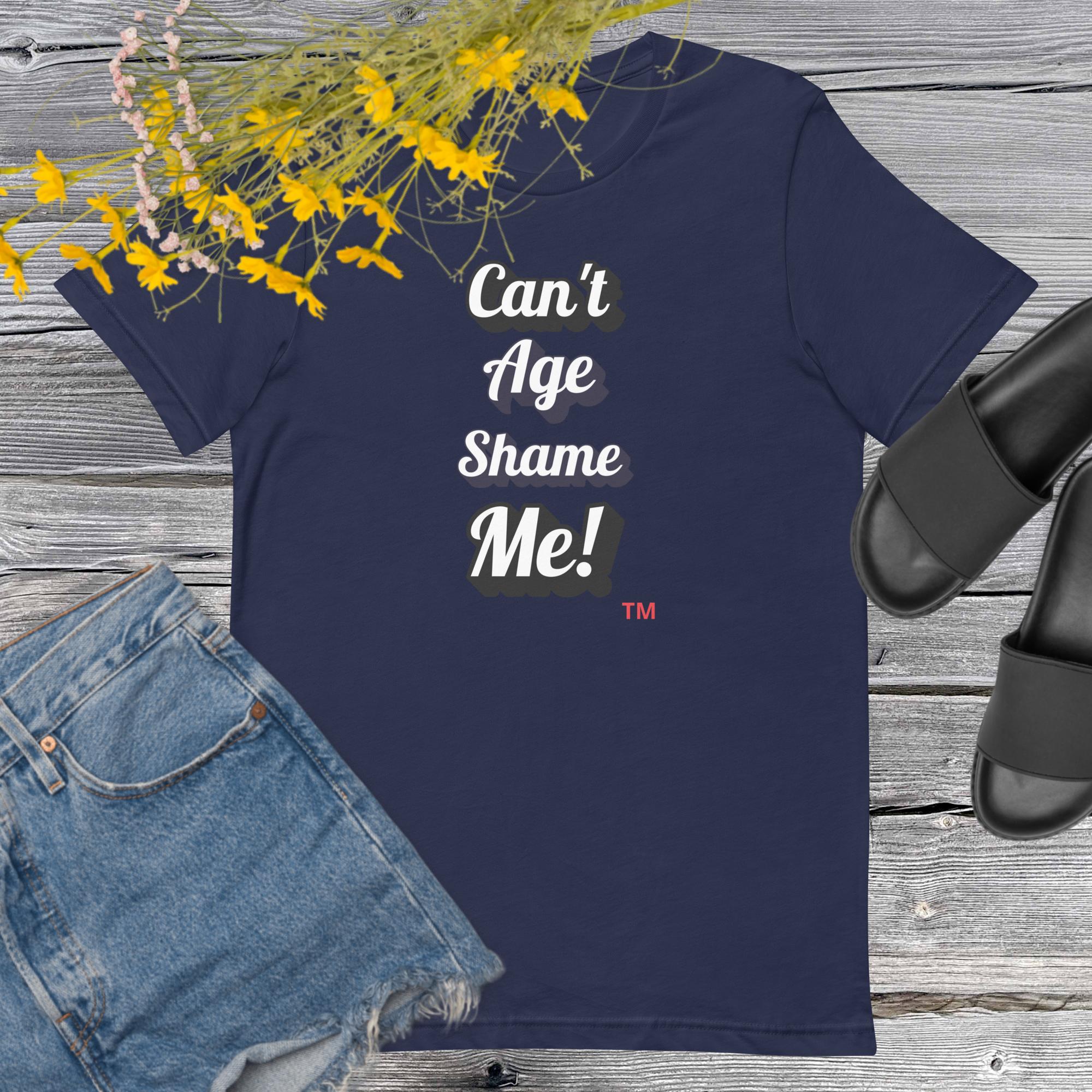 Navy blue t-shirt with 'Can't Age Shame Me!' text on a wooden surface with denim shorts and black sandals.