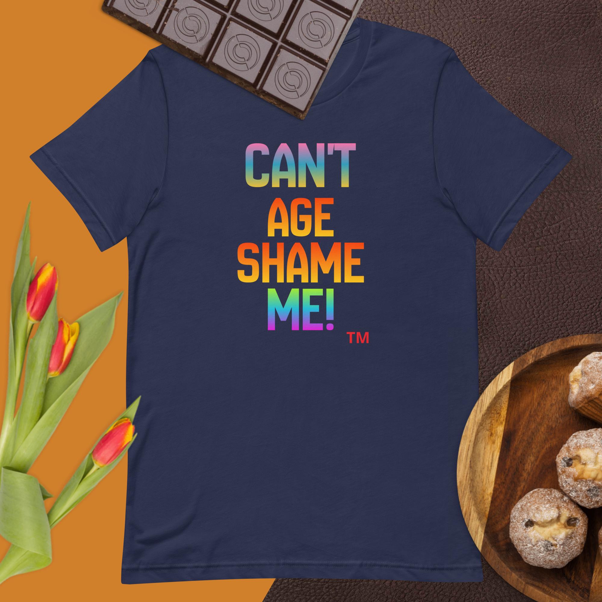 Navy blue t-shirt with colorful text 'CAN'T AGE SHAME ME!' on a brown surface with tulips and cookies.