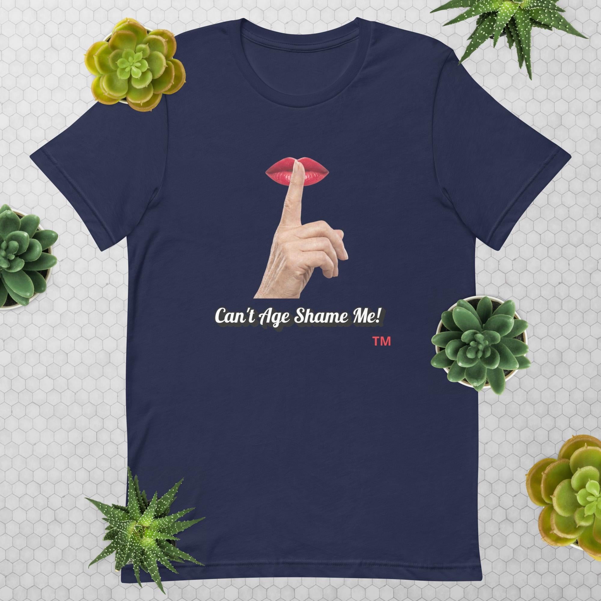 Navy t-shirt with graphic design of finger on mouth and text 'CAN'T AGE SHAME ME!' text logo on a light gray background with succulents.