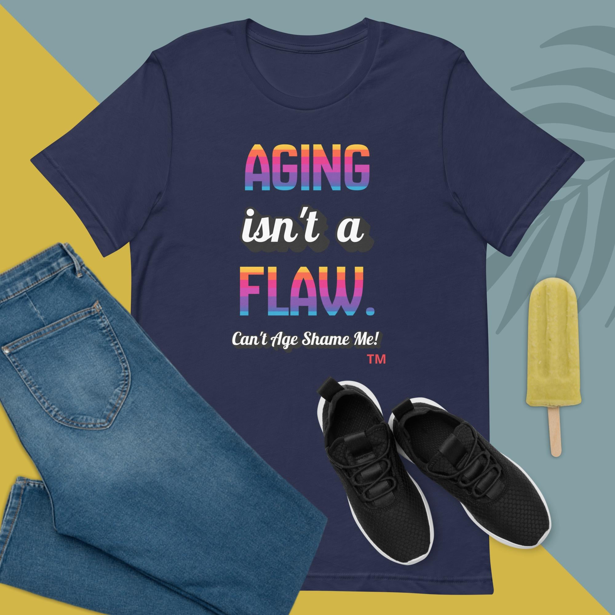 Navy t-shirt with 'Aging isn't a flaw' text, paired with jeans and sneakers on a colorful background.