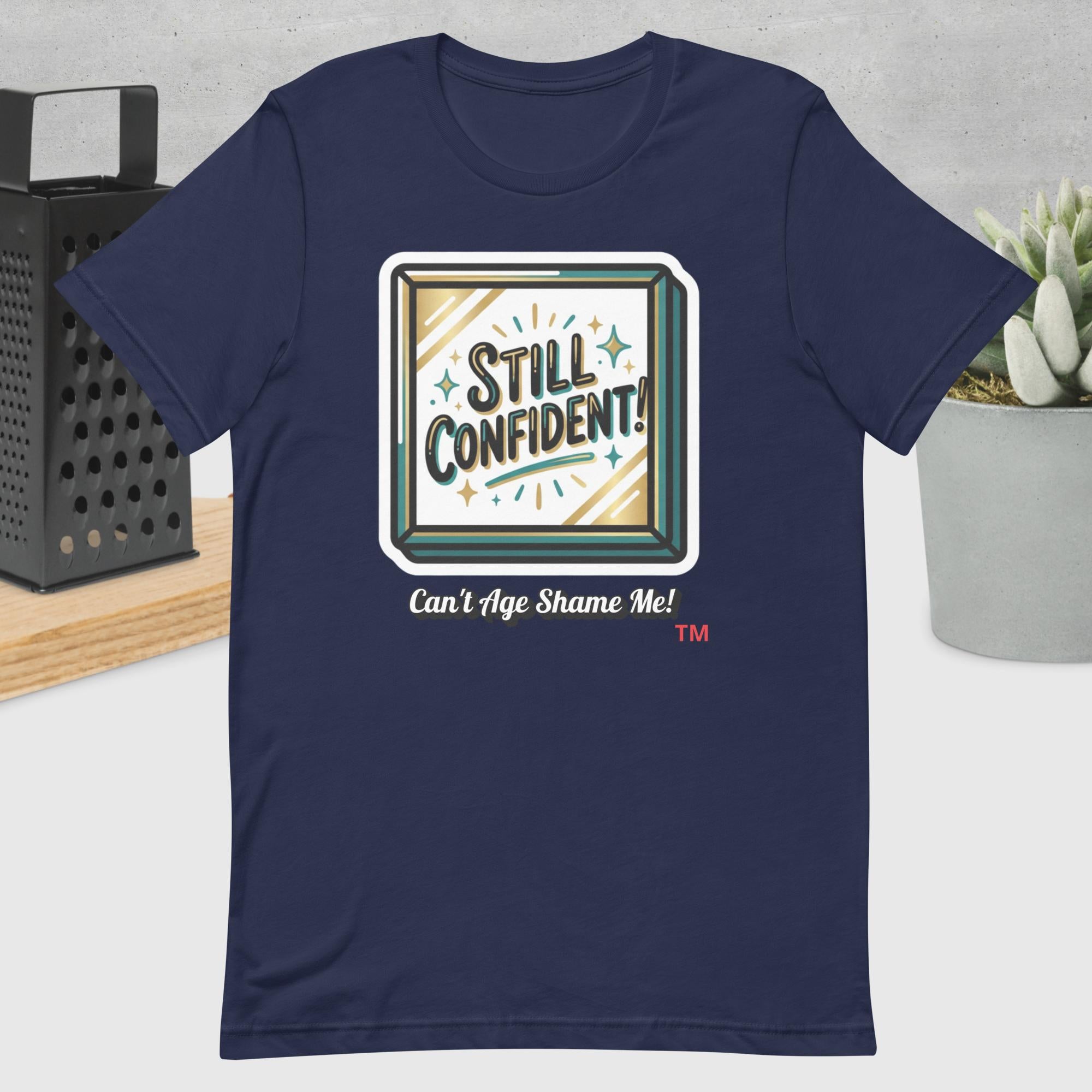 Navy blue t-shirt with 'Still Confident! Can't Age Shame Me!' graphic design on a neutral background.