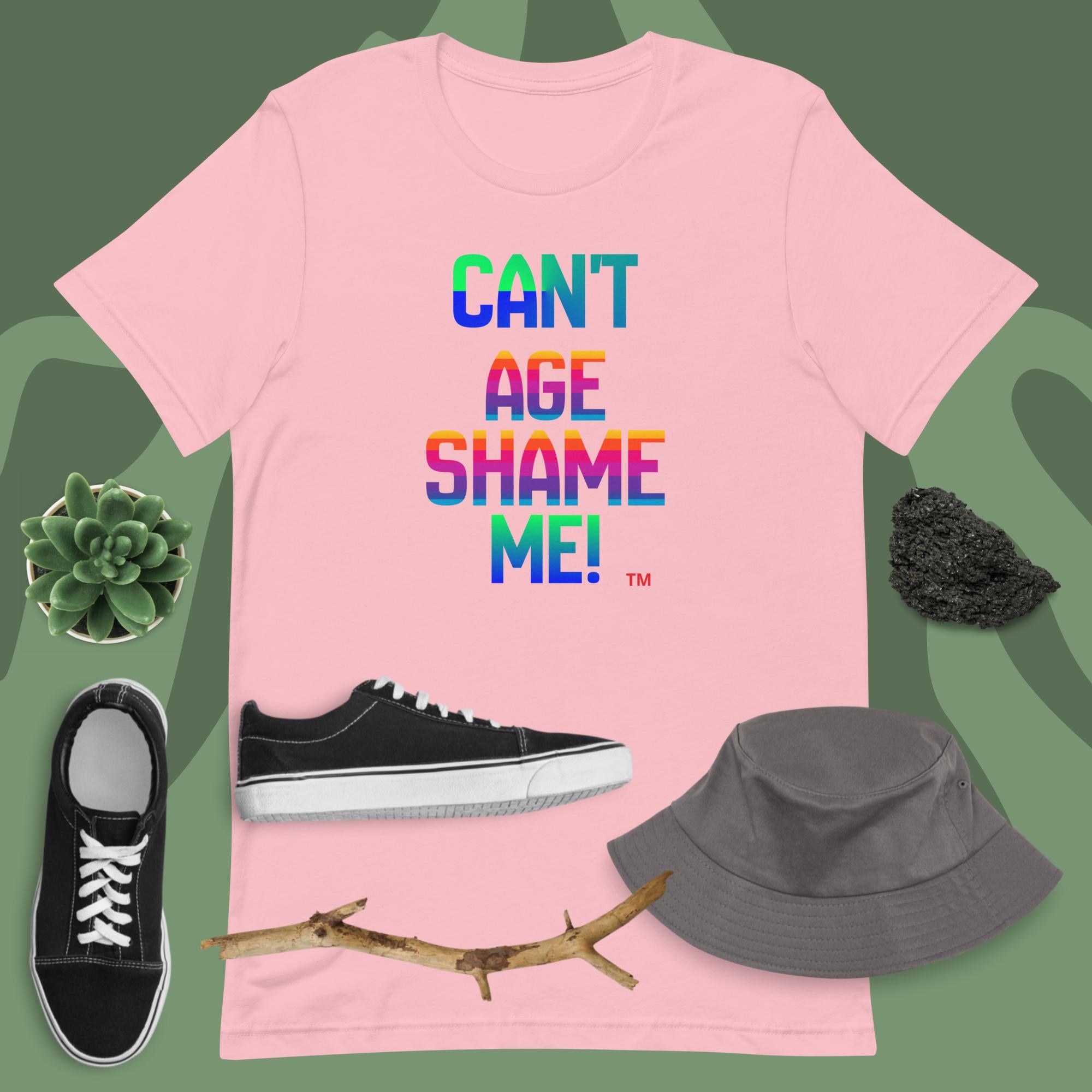 Pink t-shirt with colorful text, black sneakers, gray bucket hat, and branch on a green background