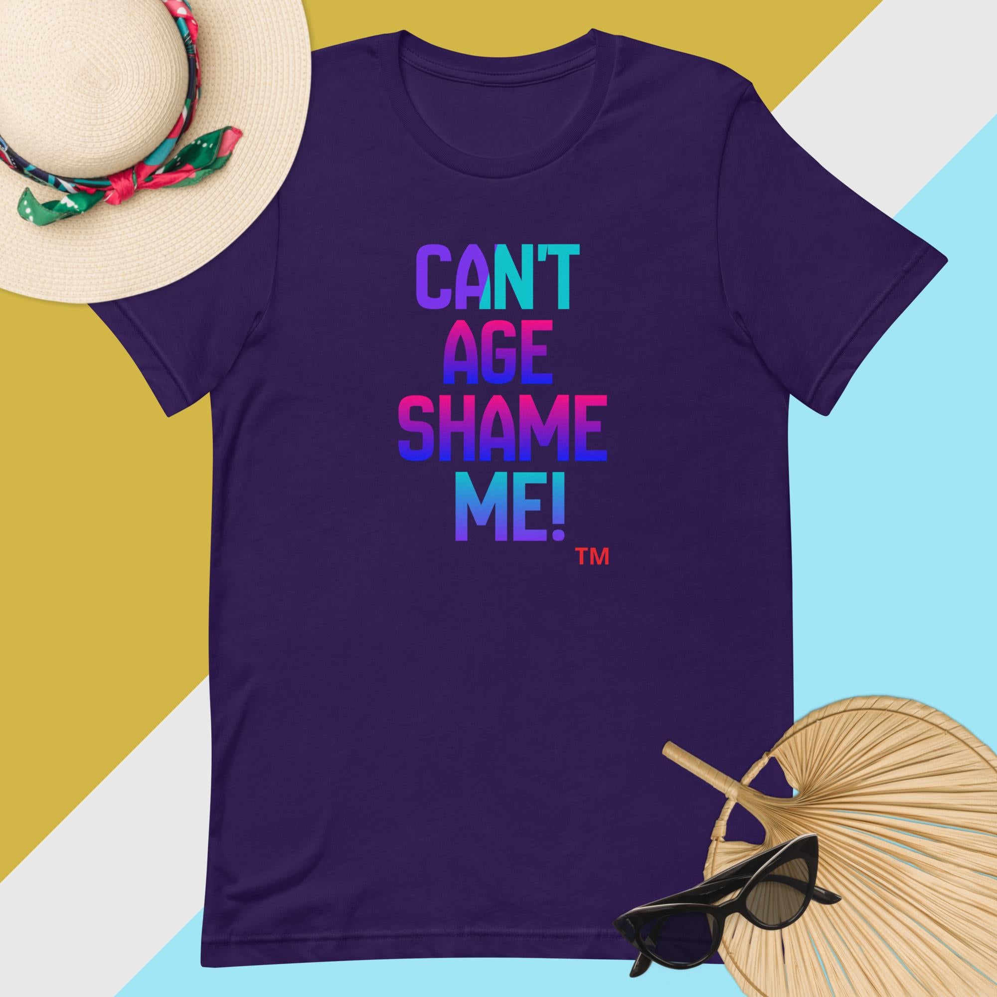 Purple t-shirt with colorful text 'CAN'T AGE SHAME ME!' on a multicolored background with accessories.