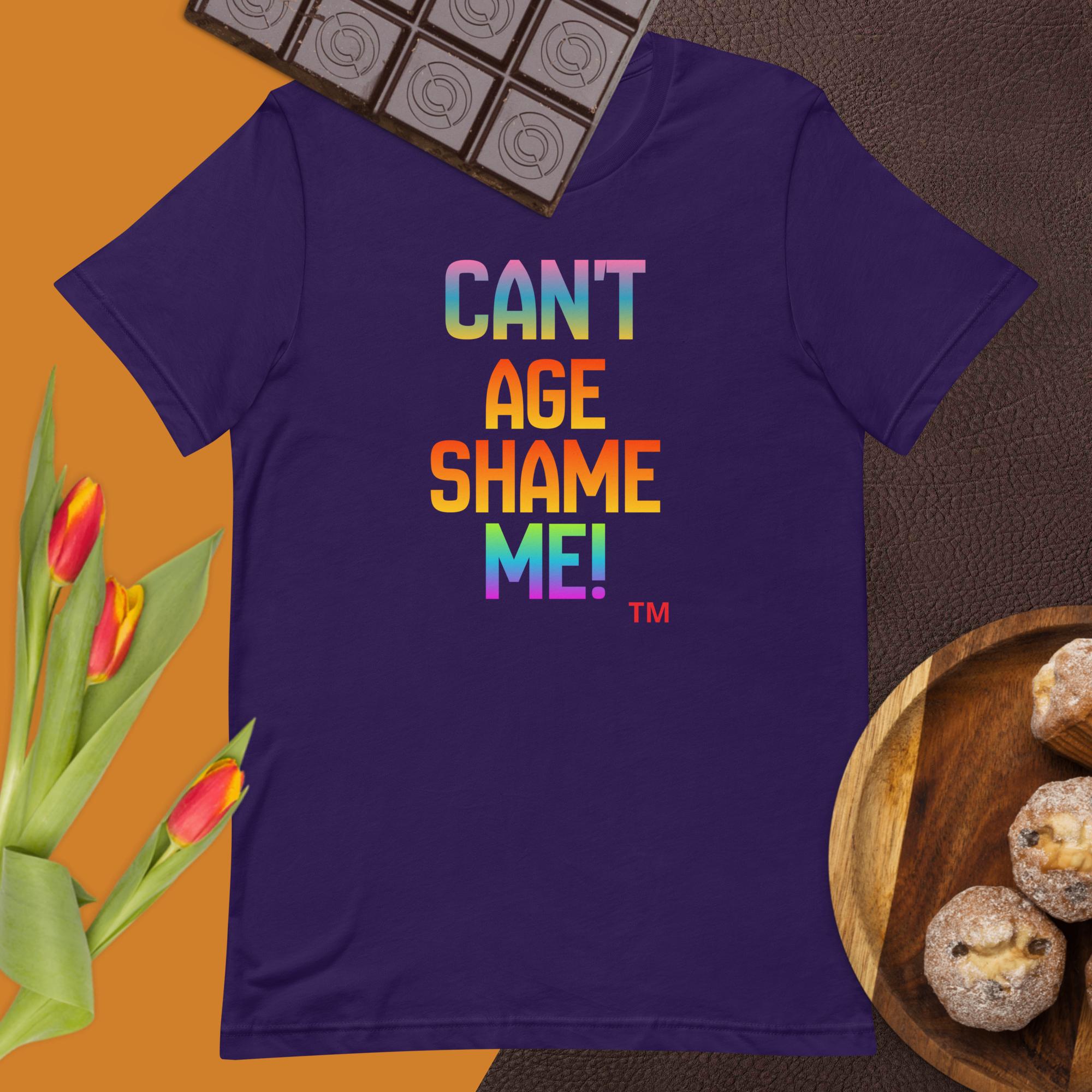 Purple t-shirt with colorful text 'CAN'T AGE SHAME ME!' on a table with tulips and cookies.